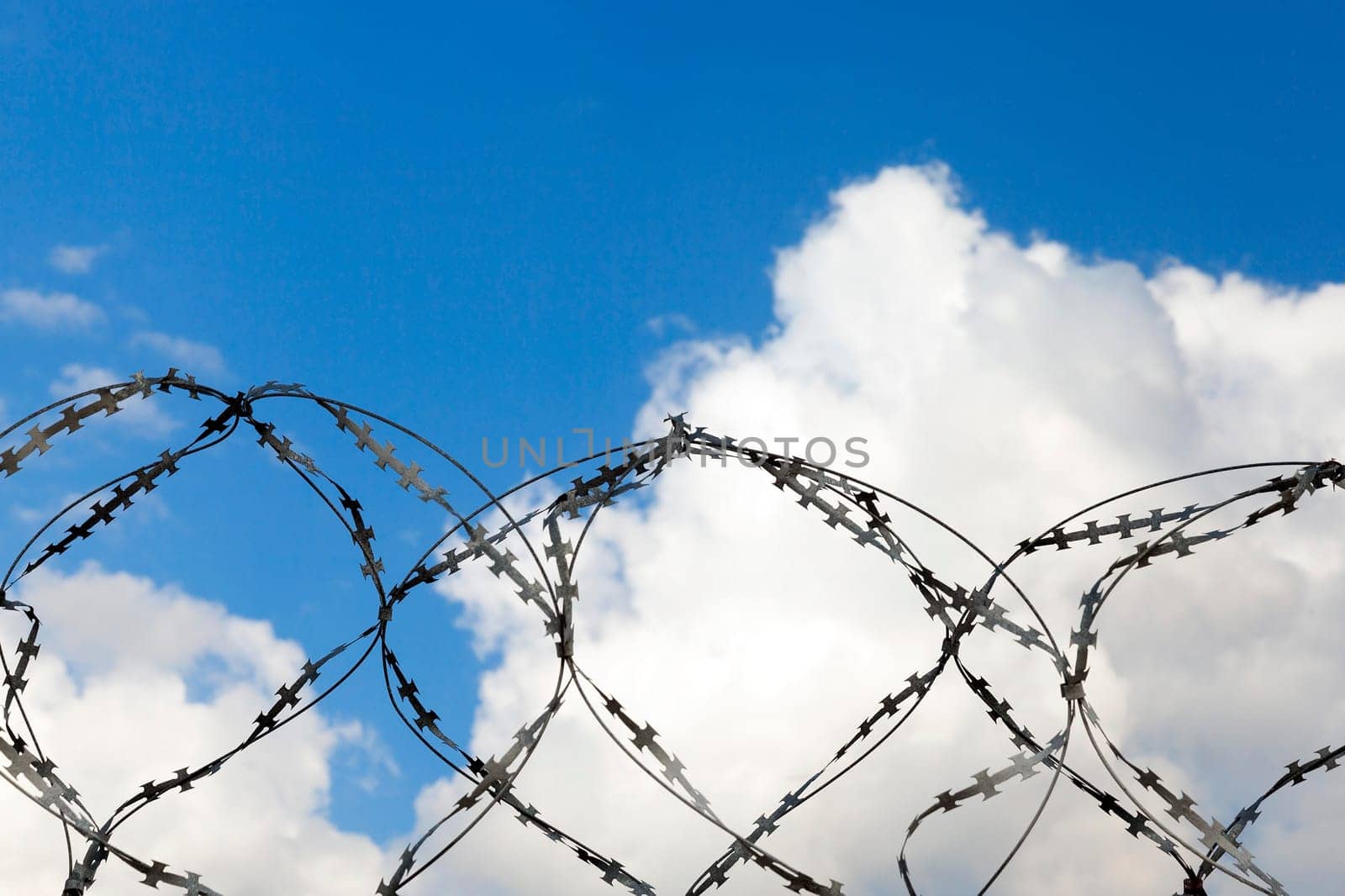 several rows of old barbed wire attached to the wall. Against the background of blue sky