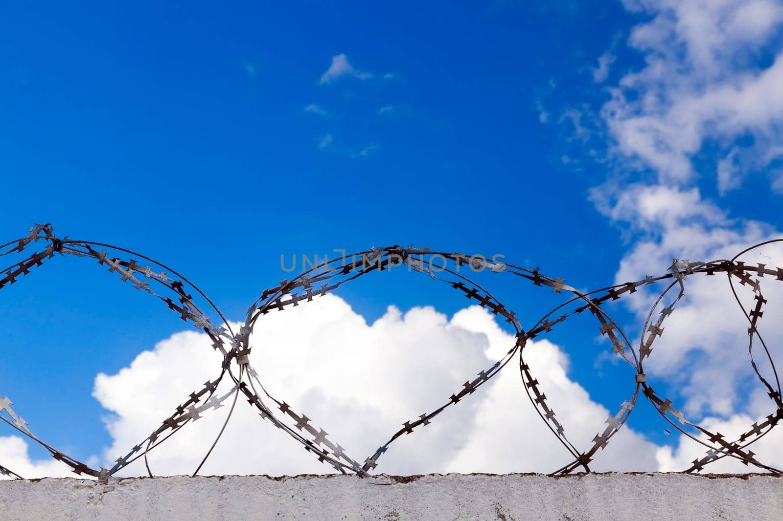 several rows of old barbed wire attached to the wall. Against the background of blue sky