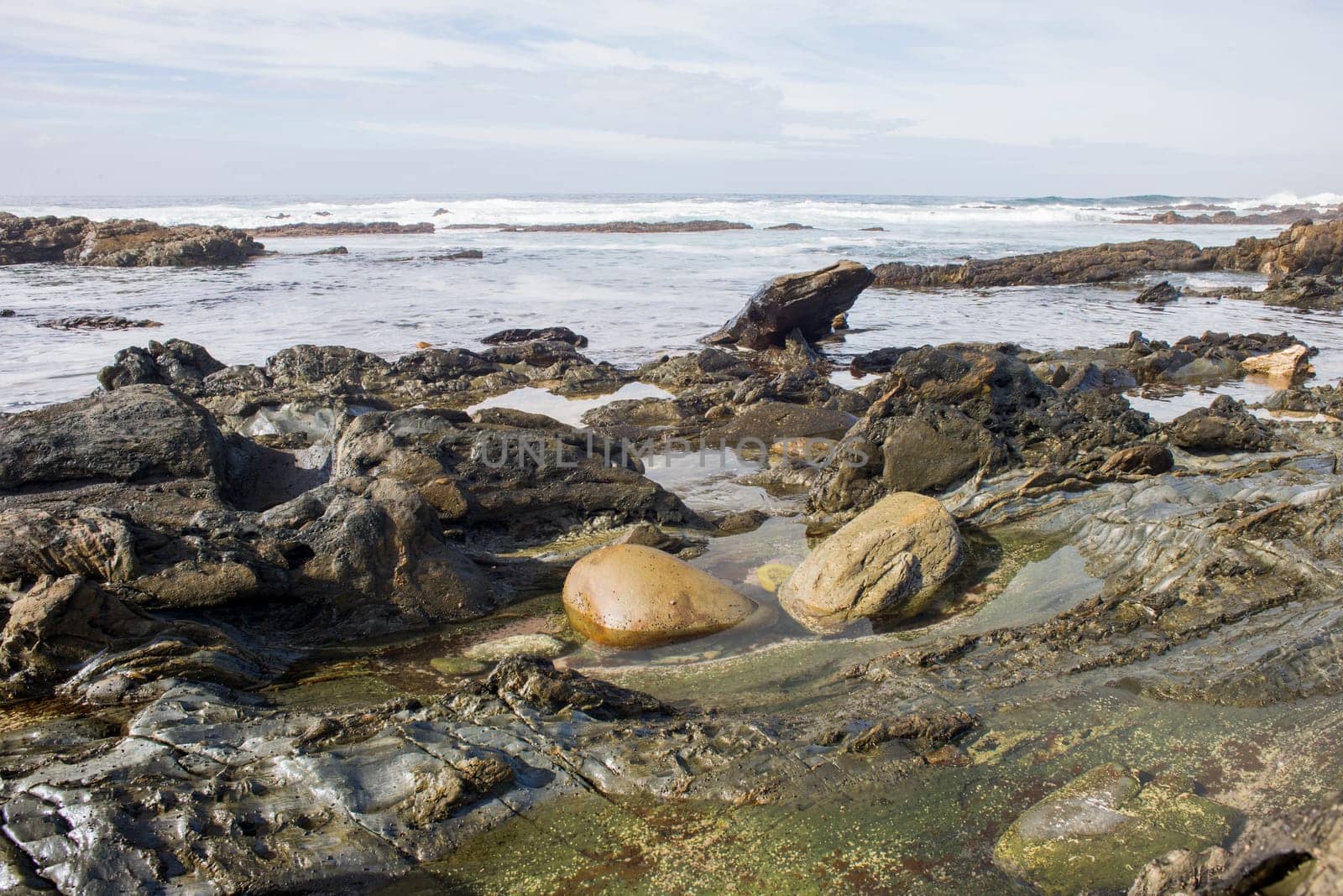 Two big boulders lie in the water of a rock pool on a rugged coastline.