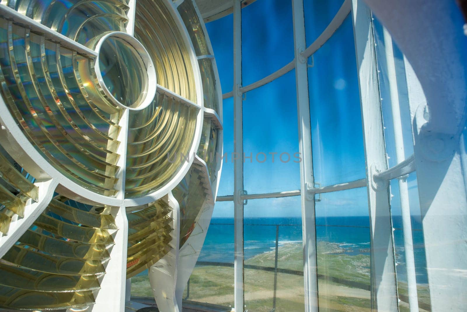 An up close view of the light of the Cape Agulhas lightouse with a view of the ocean in the background.