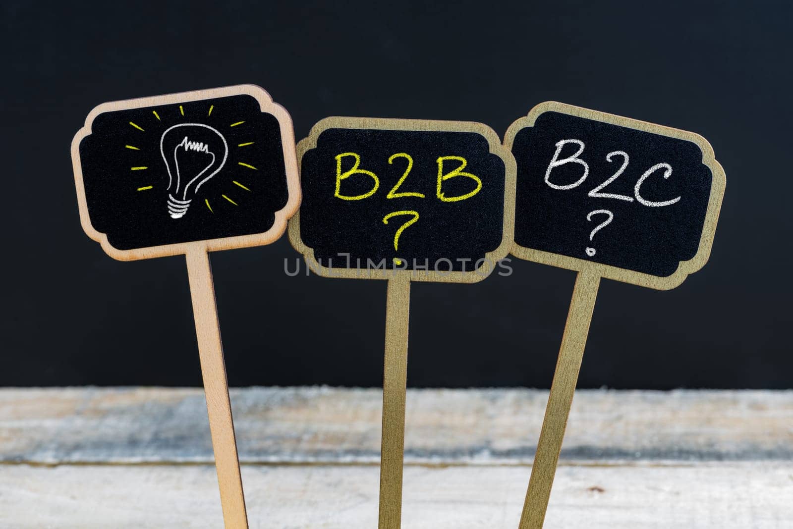 Concept message B2B as Business To Business, B2C as Business To Consumer and light bulb as symbol for idea written with chalk on wooden mini blackboard labels, defocused chalkboard and wood table in background