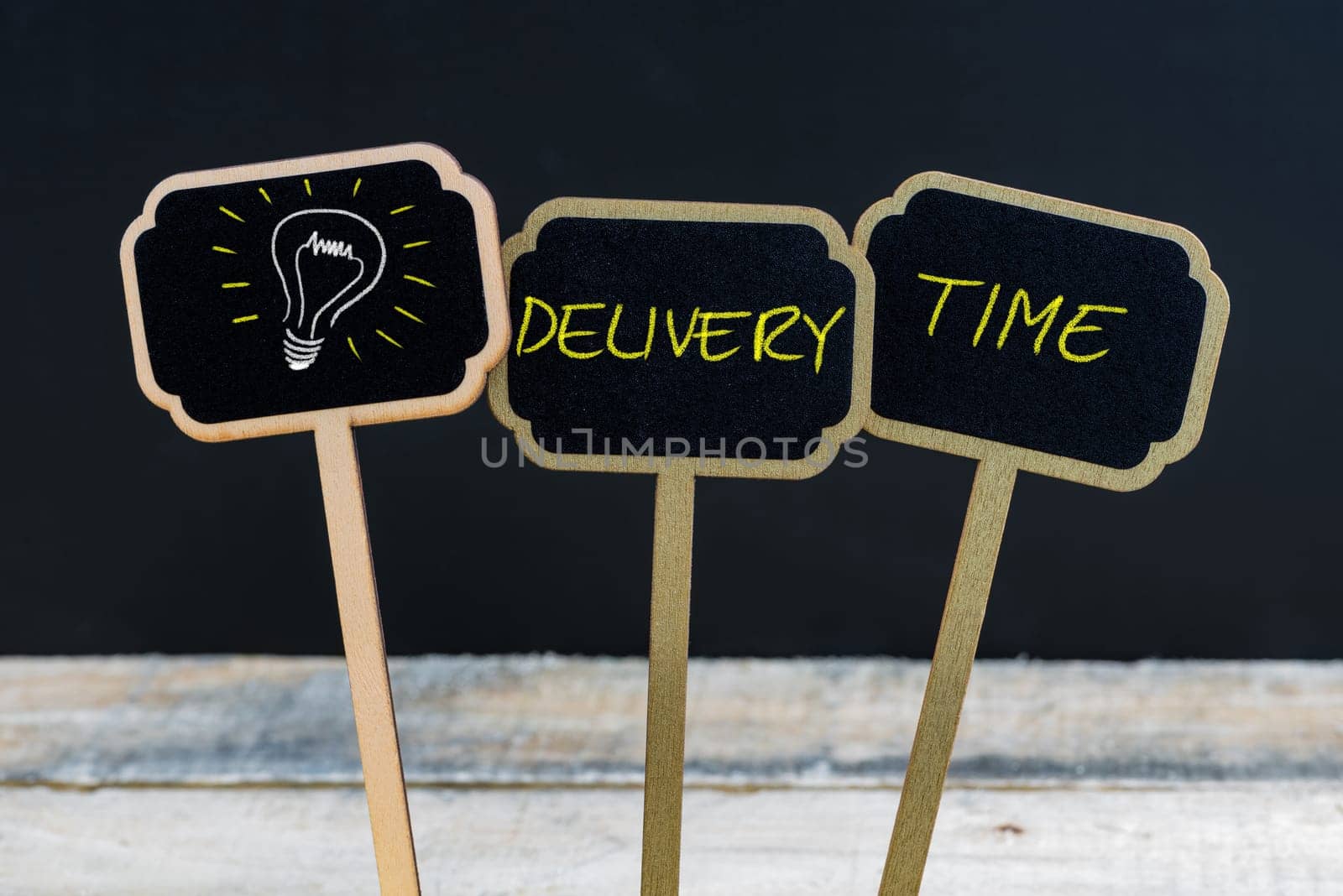 Concept message DELIVERY TIME and light bulb as symbol for idea written with chalk on wooden mini blackboard labels, defocused chalkboard and wood table in background