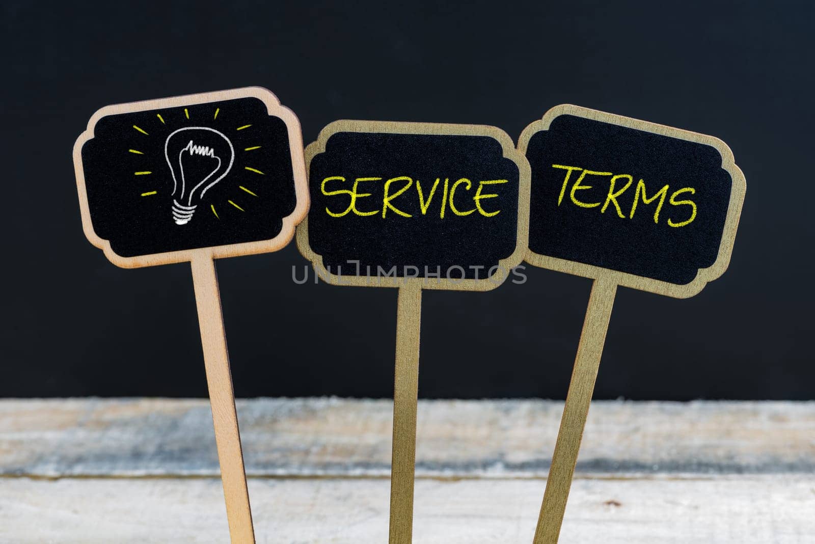 Concept message SERVICE TERMS and light bulb as symbol for idea written with chalk on wooden mini blackboard labels, defocused chalkboard and wood table in background