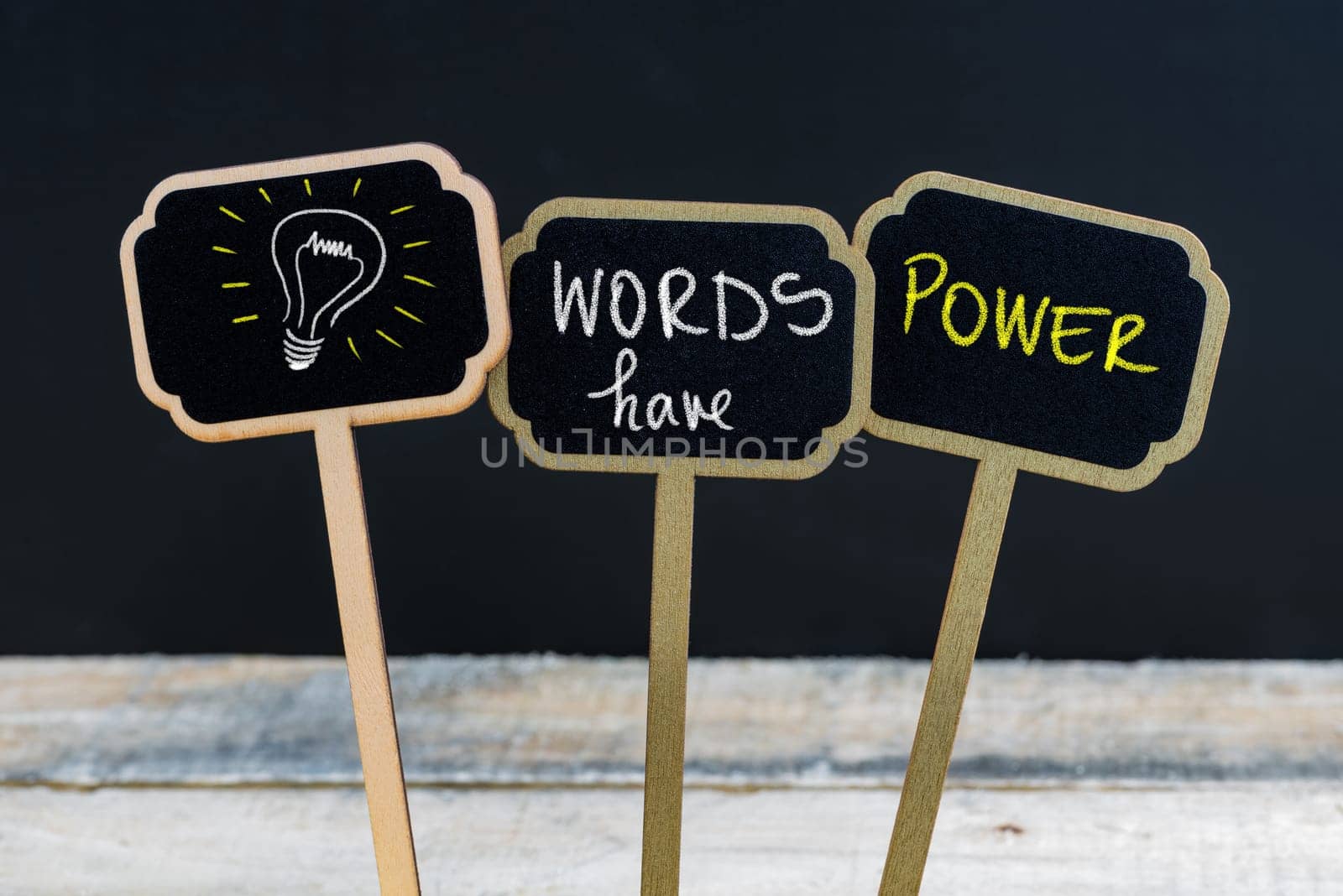 Concept message WORDS HAVE POWER and light bulb as symbol for idea written with chalk on wooden mini blackboard labels, defocused chalkboard and wood table in background