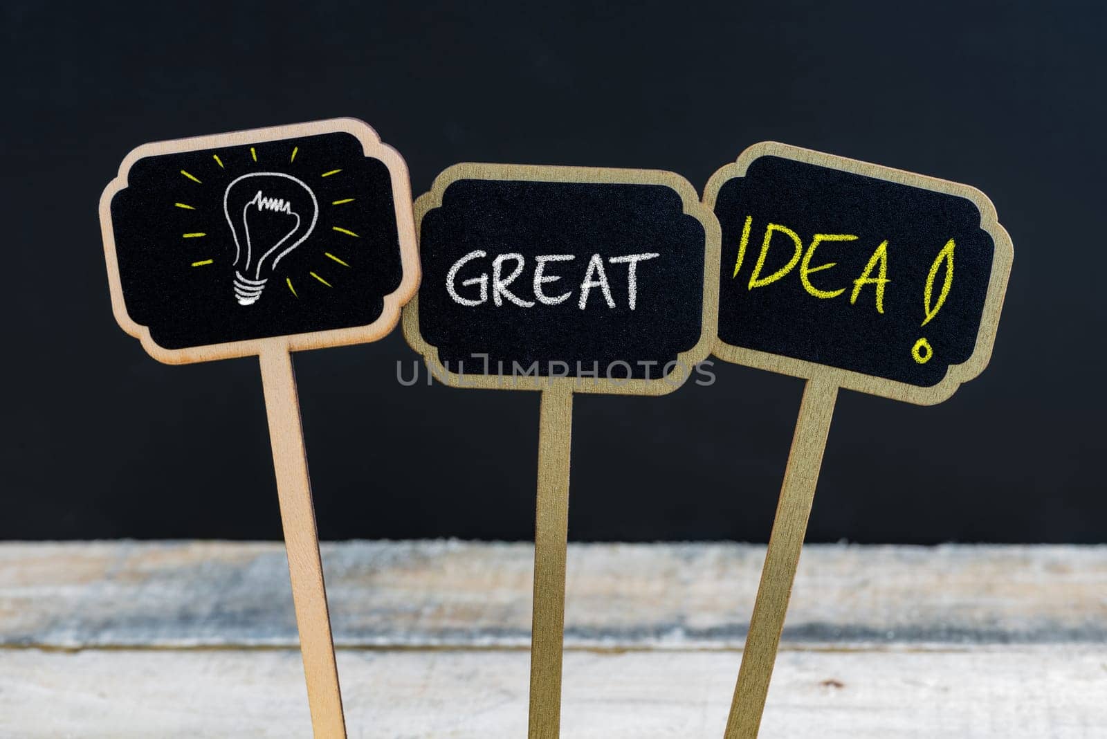 Concept message GREAT IDEA and light bulb as symbol for idea written with chalk on wooden mini blackboard labels, defocused chalkboard and wood table in background