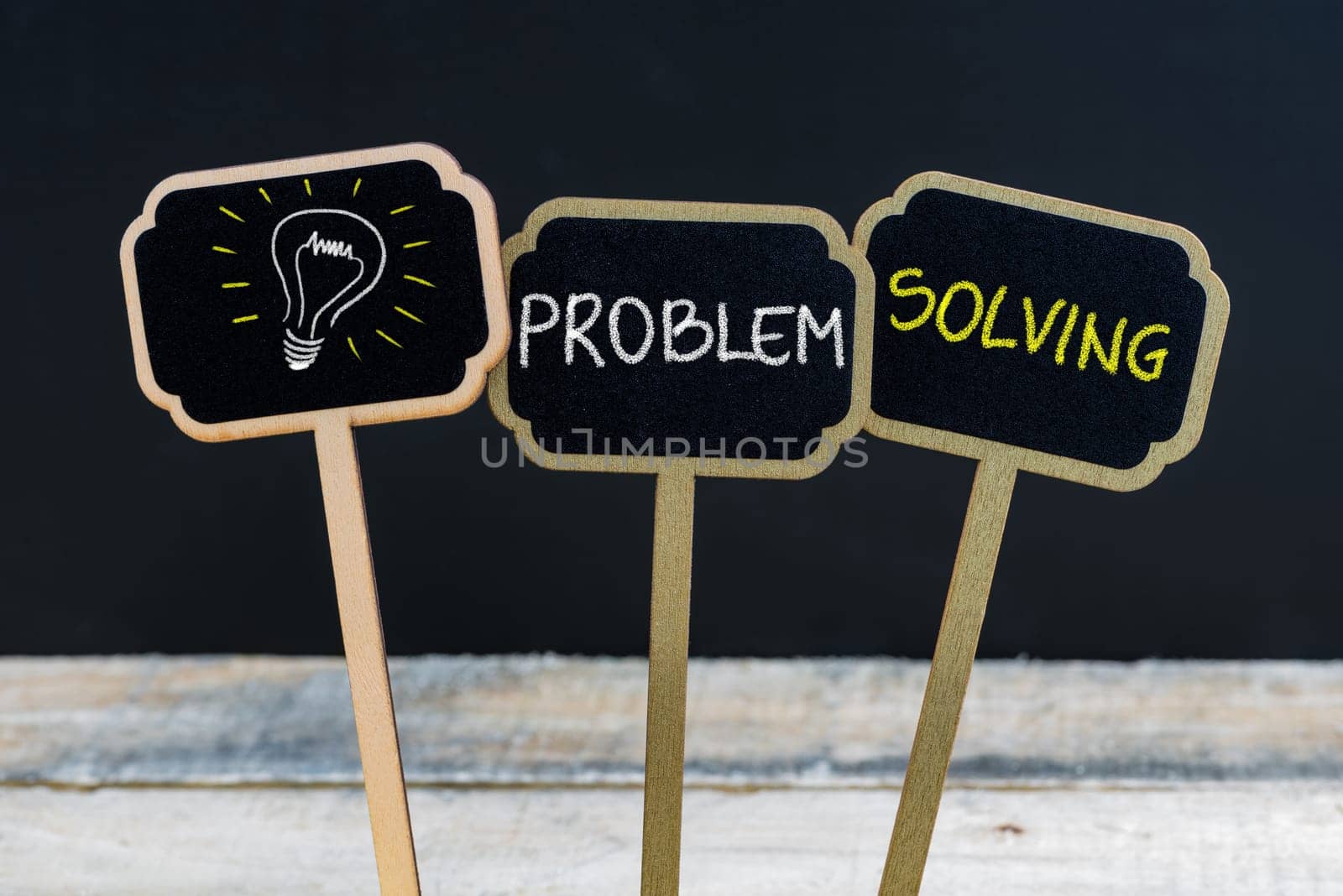 Concept message PROBLEM SOLVING and light bulb as symbol for idea written with chalk on wooden mini blackboard labels, defocused chalkboard and wood table in background