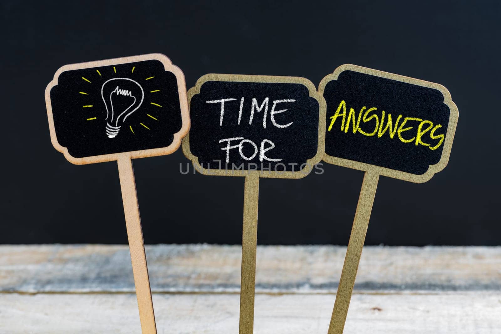 Concept message TIME FOR ANSWERS and light bulb as symbol for idea written with chalk on wooden mini blackboard labels, defocused chalkboard and wood table in background