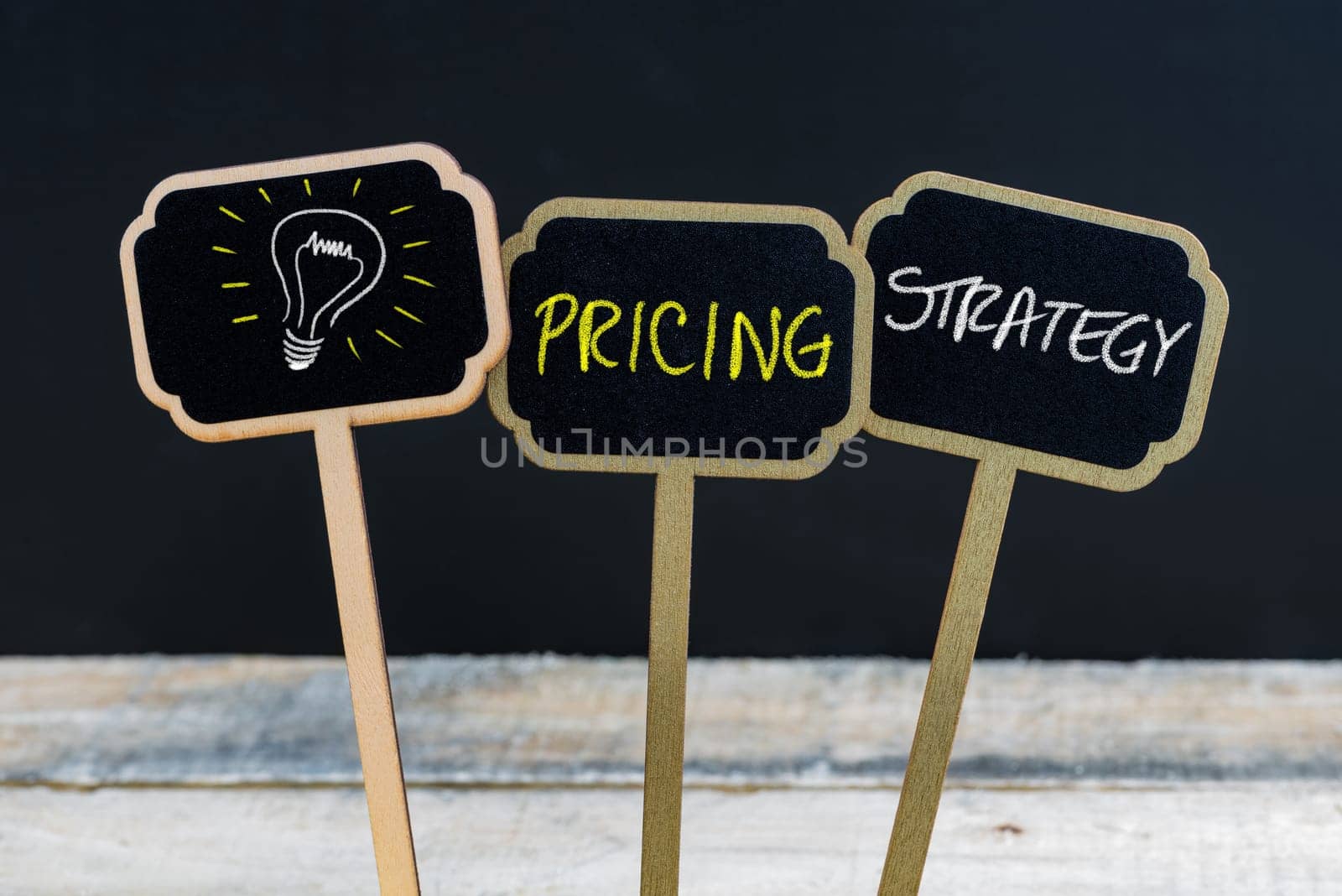 Concept message PRICING STRATEGY and light bulb as symbol for idea written with chalk on wooden mini blackboard labels, defocused chalkboard and wood table in background