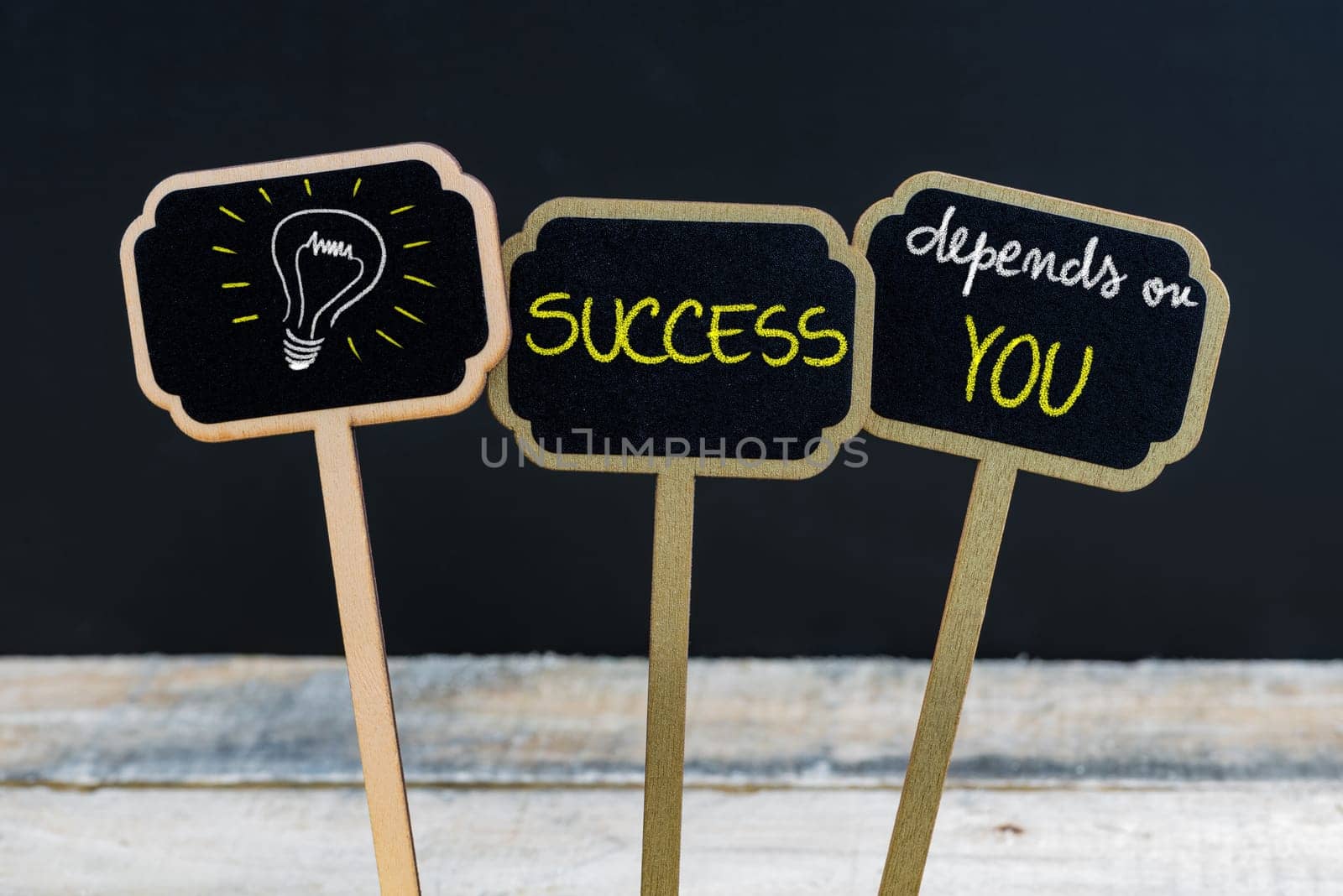Concept message SUCCESS DEPENDS ON YOU and light bulb as symbol for idea written with chalk on wooden mini blackboard labels, defocused chalkboard and wood table in background