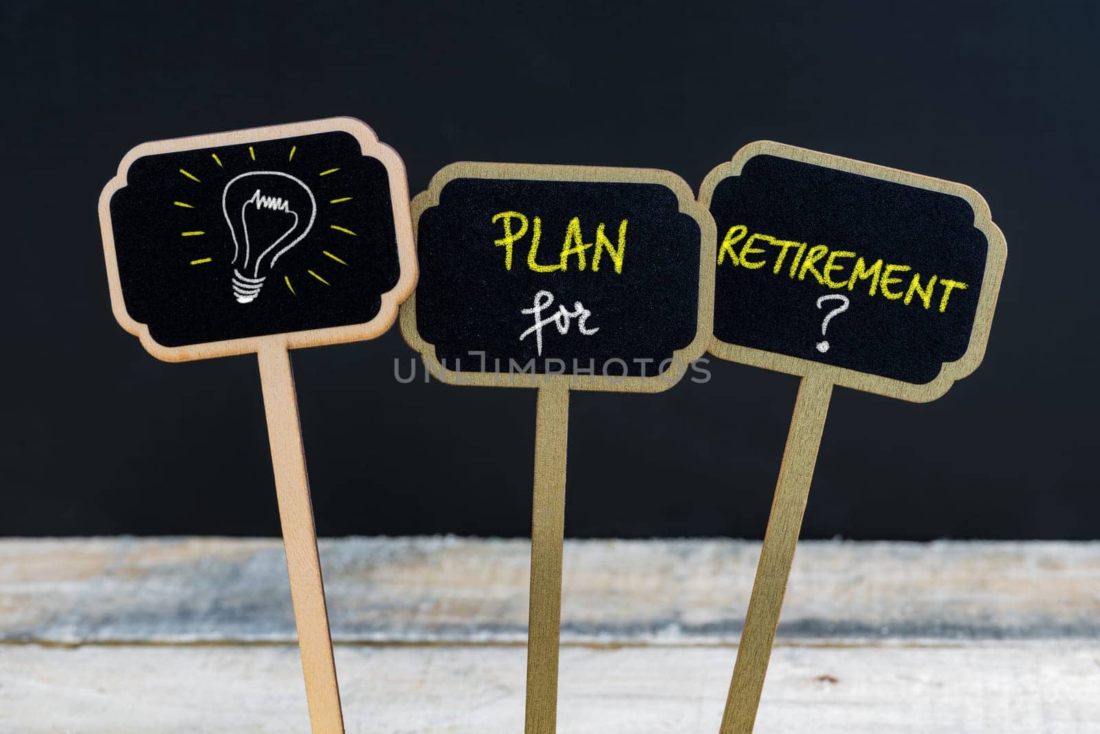 Concept message PLAN FOR RETIREMENT and light bulb as symbol for idea written with chalk on wooden mini blackboard labels, defocused chalkboard and wood table in background