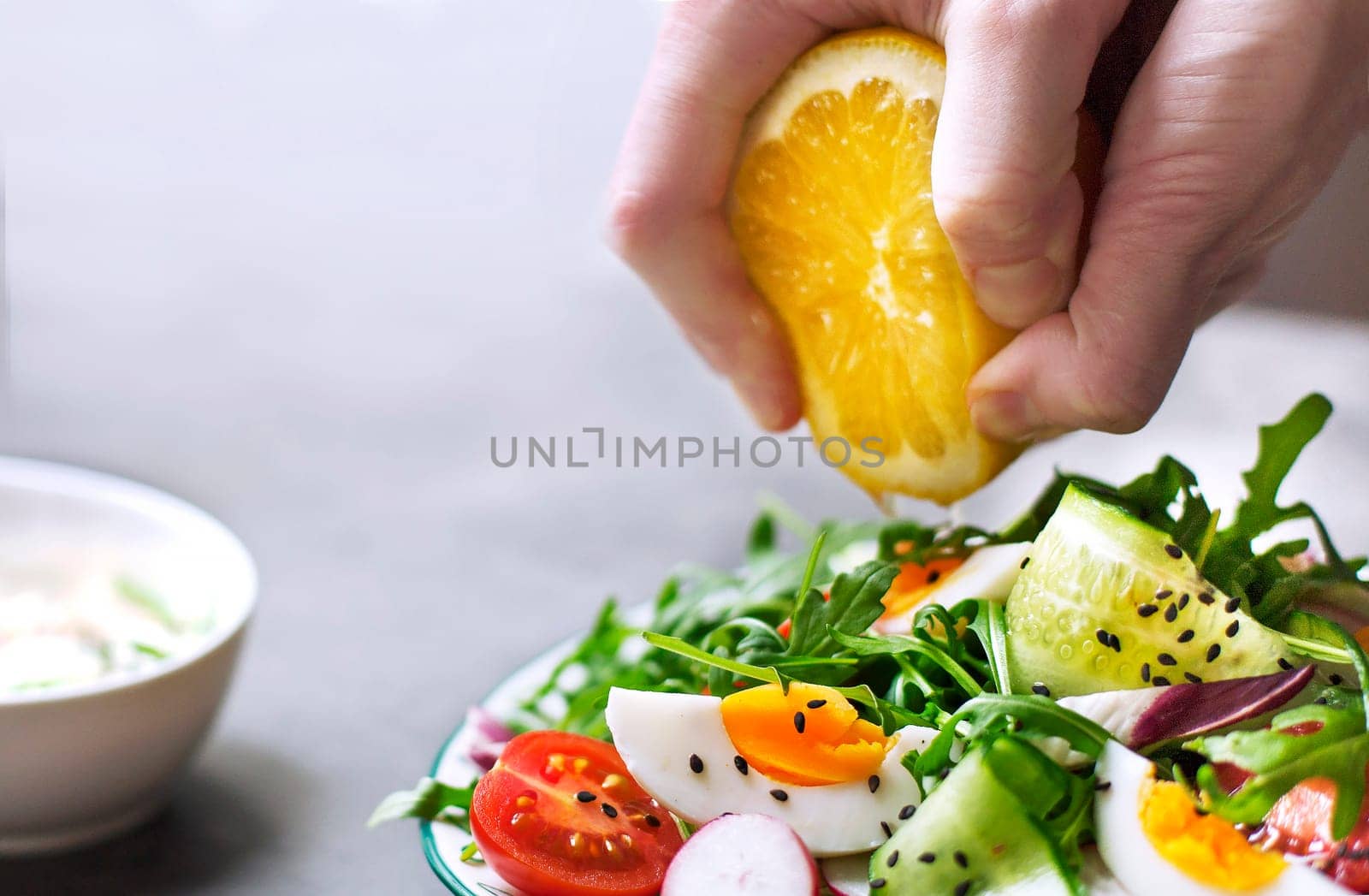 Hand squeezing juice from lemon into a Greek salad
