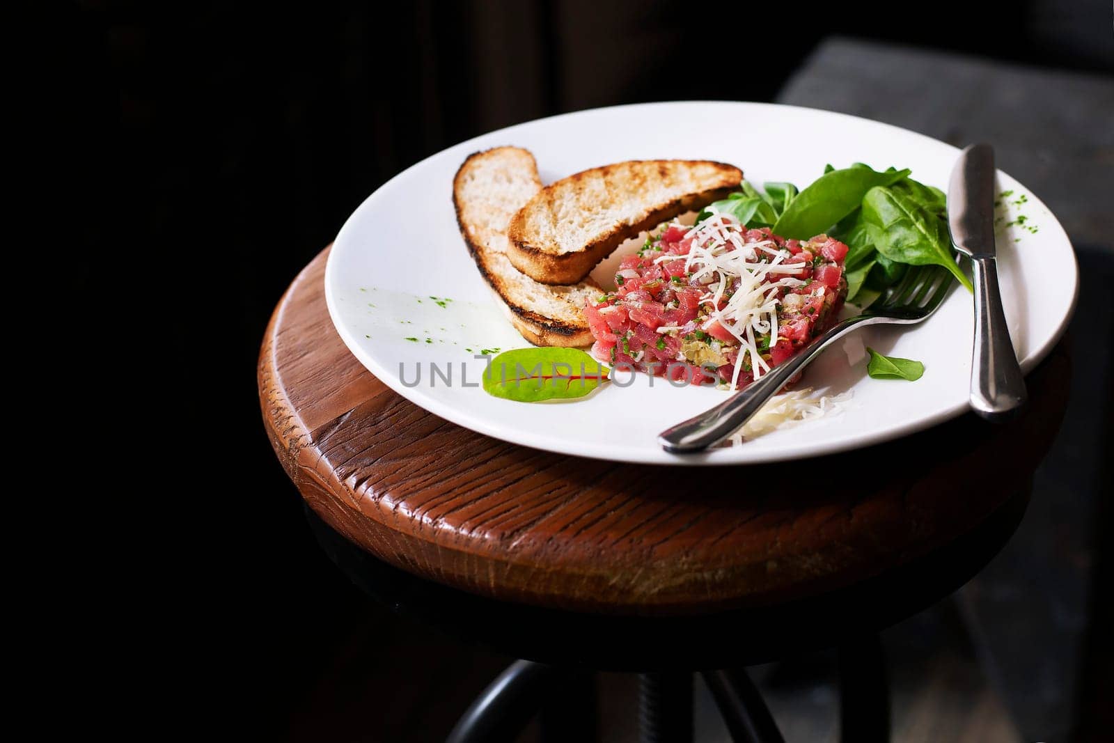 Tartare of beef with spinach on a white plate. Isolated on black.