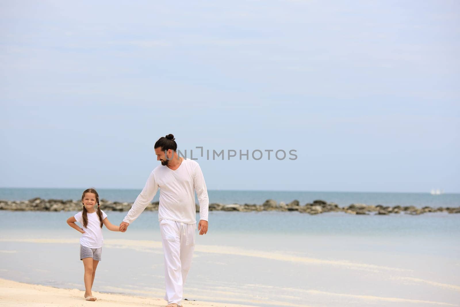 Father and daughter holding hands and walking on deserted tropical beach together happy and loving vacation