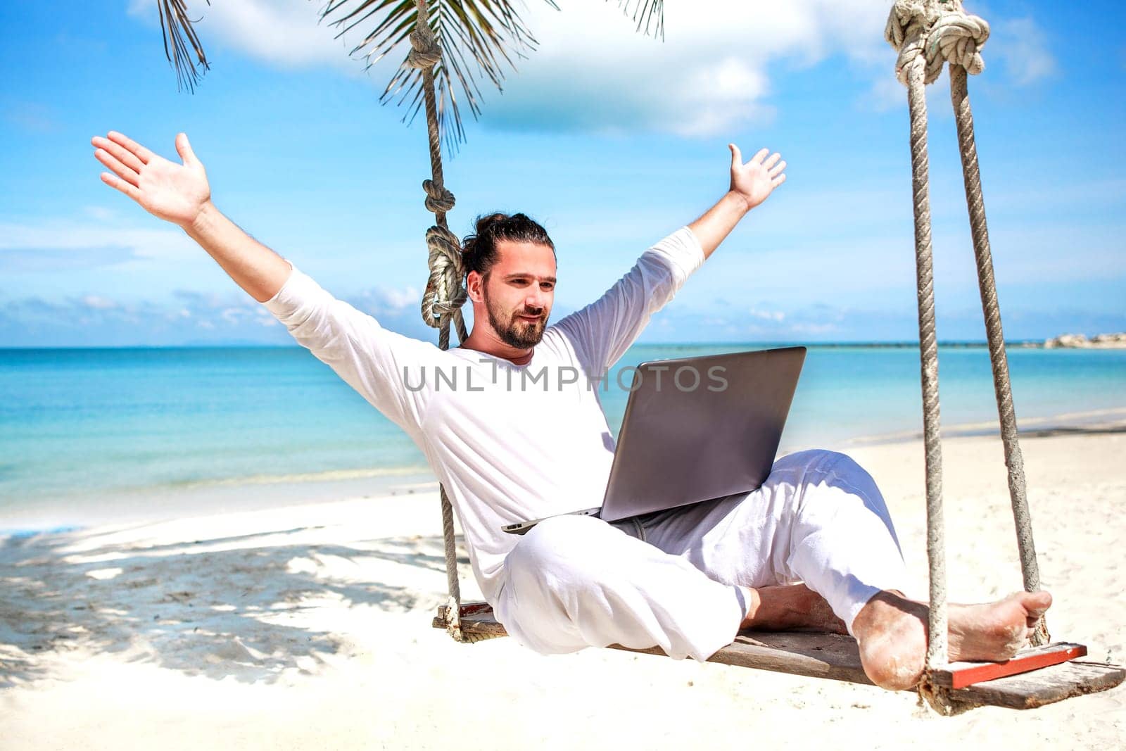 Businessman wearing white freelance sitting on beach swing with laptop