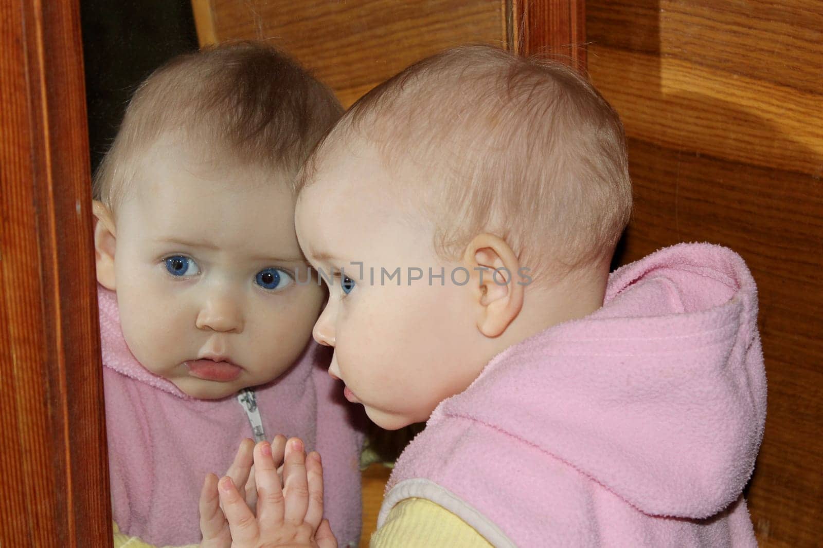 amusing baby looks at herself in front of mirror