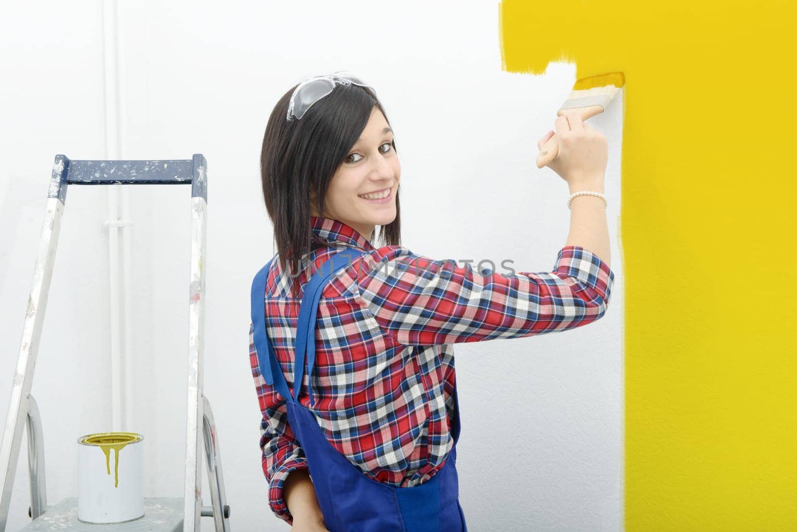 pretty young woman paints the wall yellow color