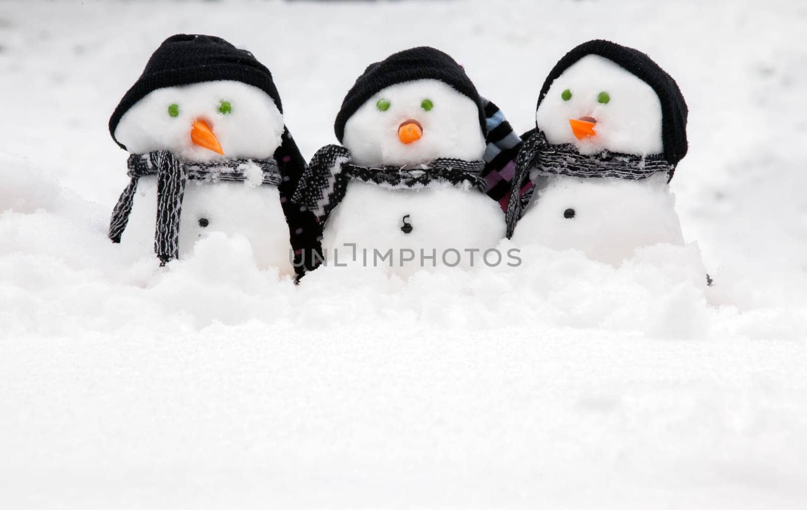 Three cute snowmen in a row sat in the snow wearing hats and scarfs. Copy space for text below