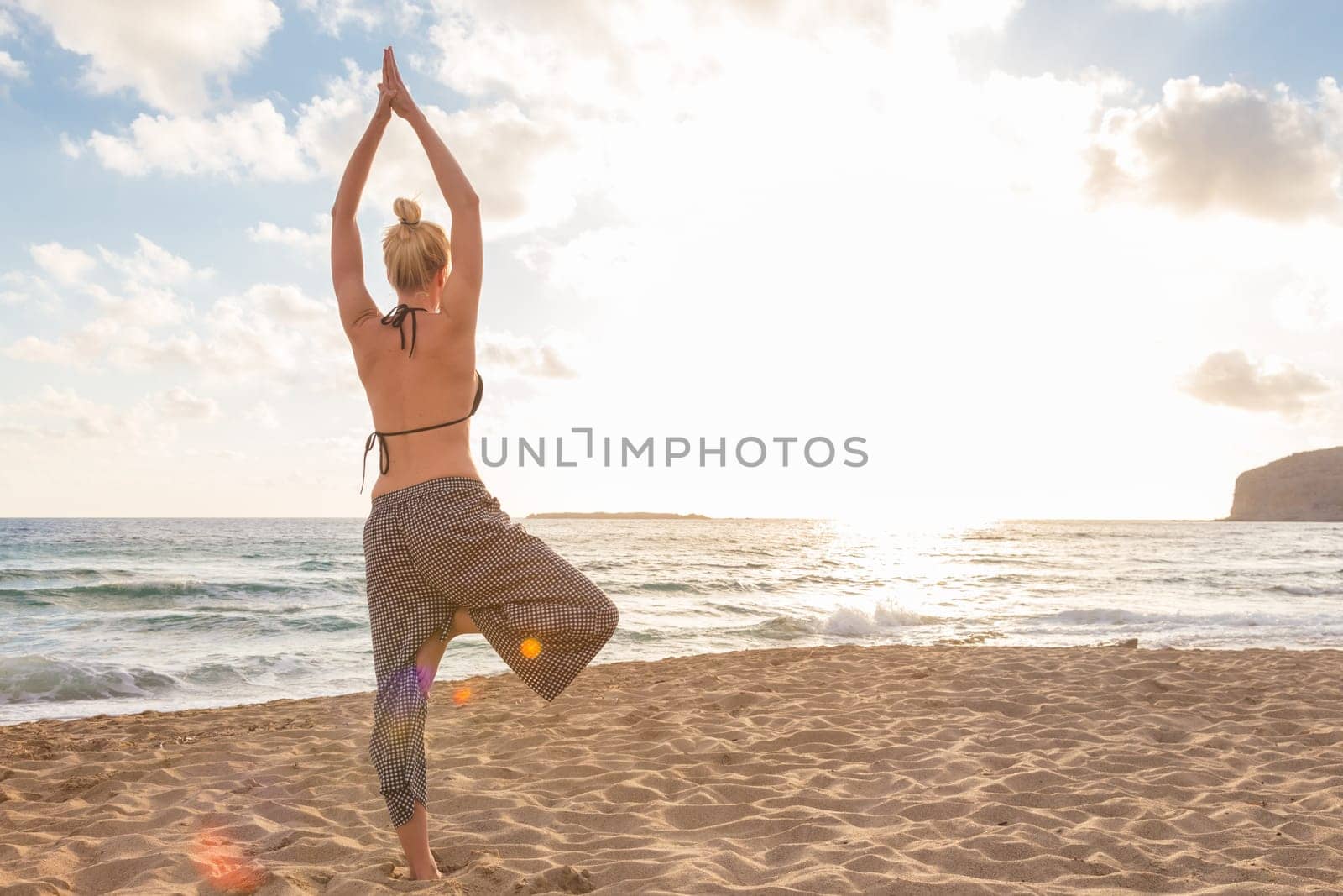 Active young woman practicing yoga on beach at sunset.