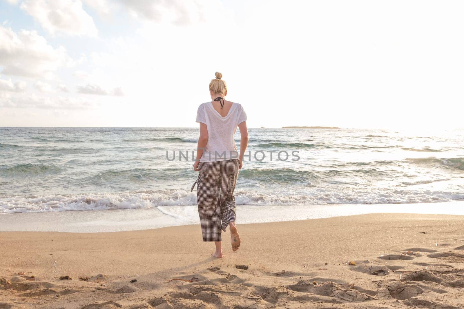 Woman walking on sand beach at golden hour. Seashore sunset walk.