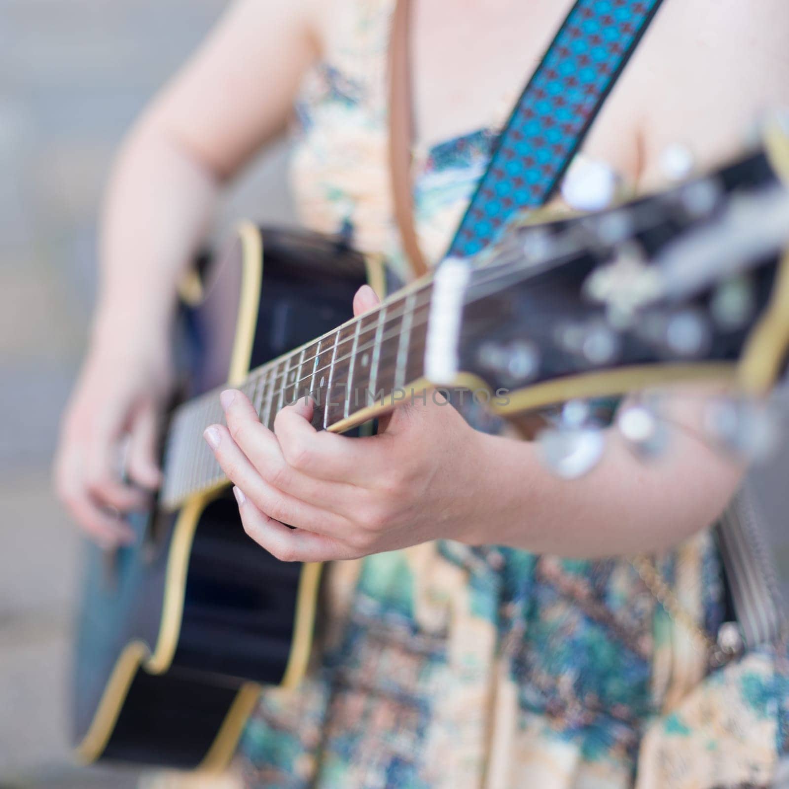 Female street musician playing guitar on sidewalk.