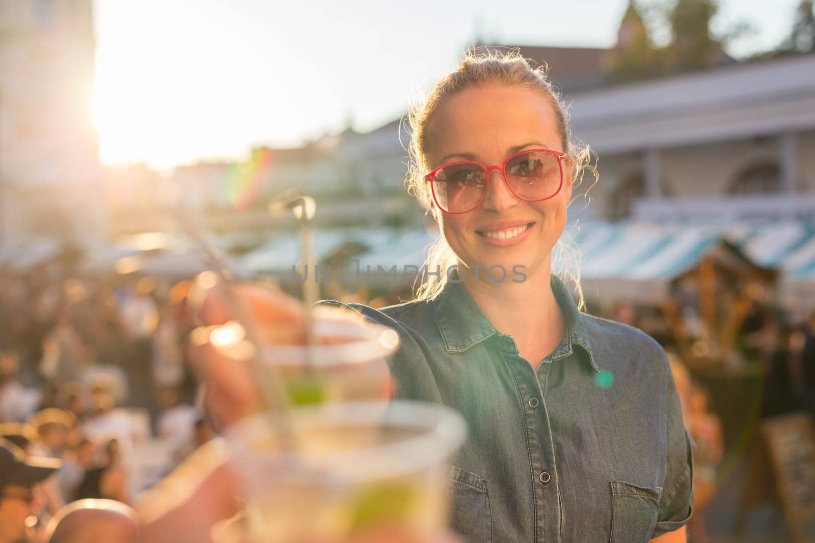Beautiful young girl toasting outdoors on Open kitchen street food festival in Ljubljana, Slovenia. Popular summer urban tourist event in capital.
