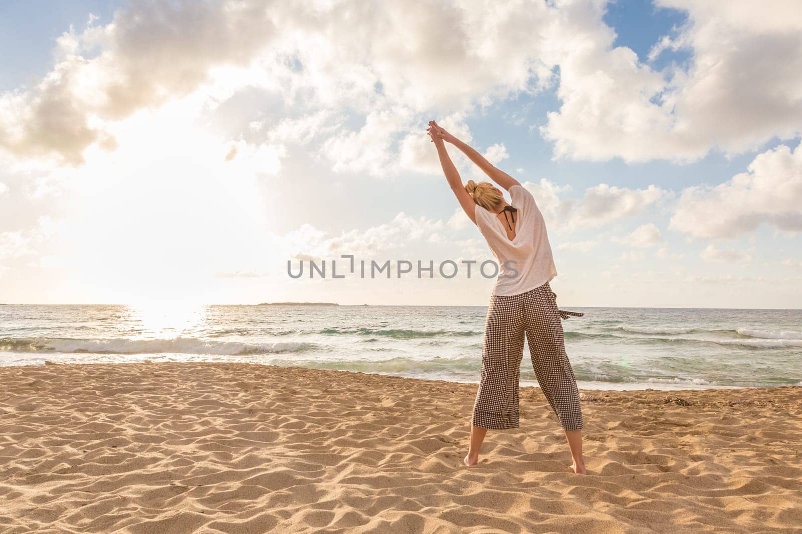 Active young woman practicing yoga on beach at sunset.