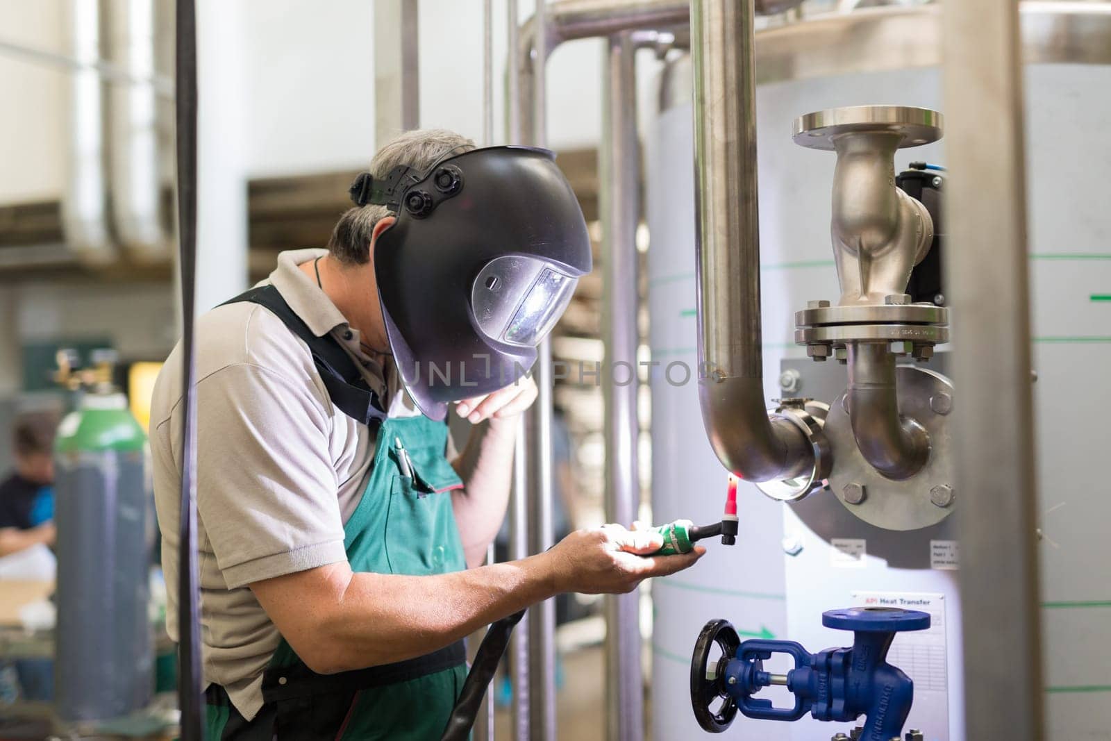 Industrial worker with protective mask welding inox elements in steel structures manufacture workshop or metal factory.