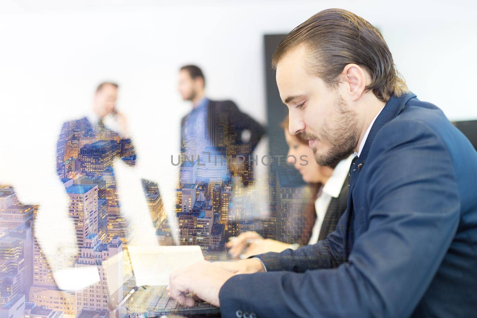 Businessman working on laptop during the meeting. Workplace in modern office with business people meeting in the background.