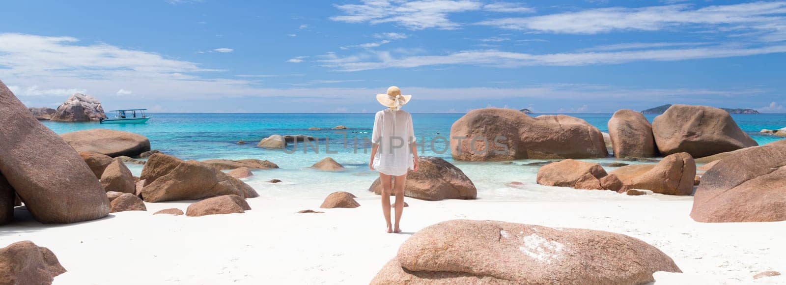 Woman wearing white loose tunic over bikini and beach hat on Anse Lazio beach on Praslin Island, Seychelles. Summer vacations on picture perfect tropical beach concept.