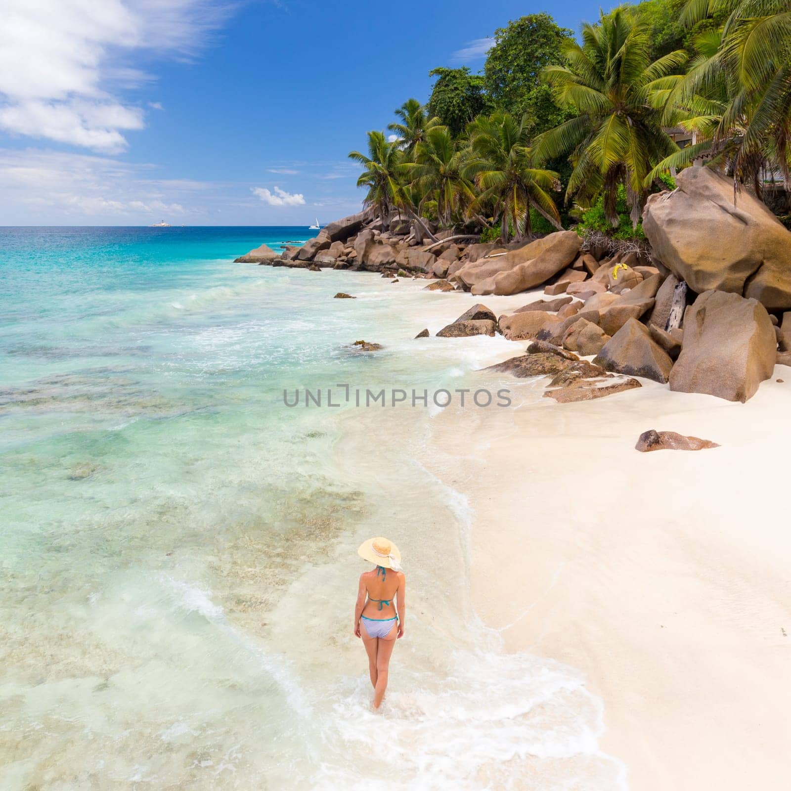 Woman wearing retro striped bikini and beach hat, enjoying amazing view on Anse Patates beach on La Digue Island, Seychelles. Summer vacations on picture perfect tropical beach concept.