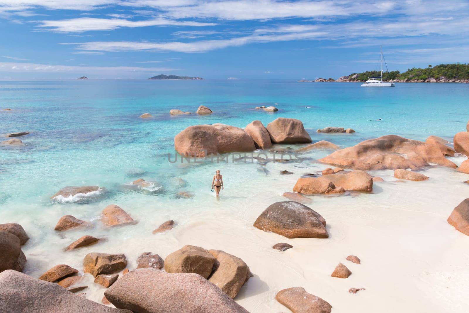 Happy woman arms rised wearing stylish bikini enjoying swimming and snorkeling at amazing Anse Lazio beach on Praslin Island, Seychelles. Summer vacations on picture perfect tropical beach concept.