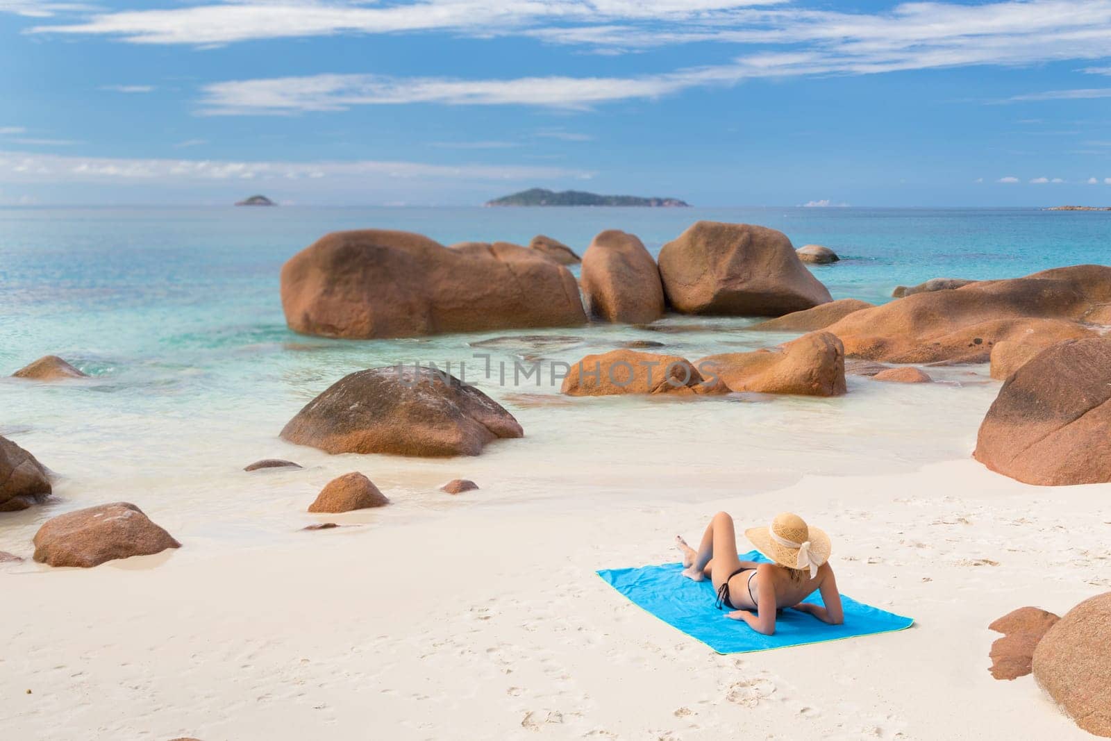 Woman wearing black bikini and beach hat, sunbathing at Anse Lazio beach on Praslin Island, Seychelles. Summer vacations on picture perfect tropical beach concept.