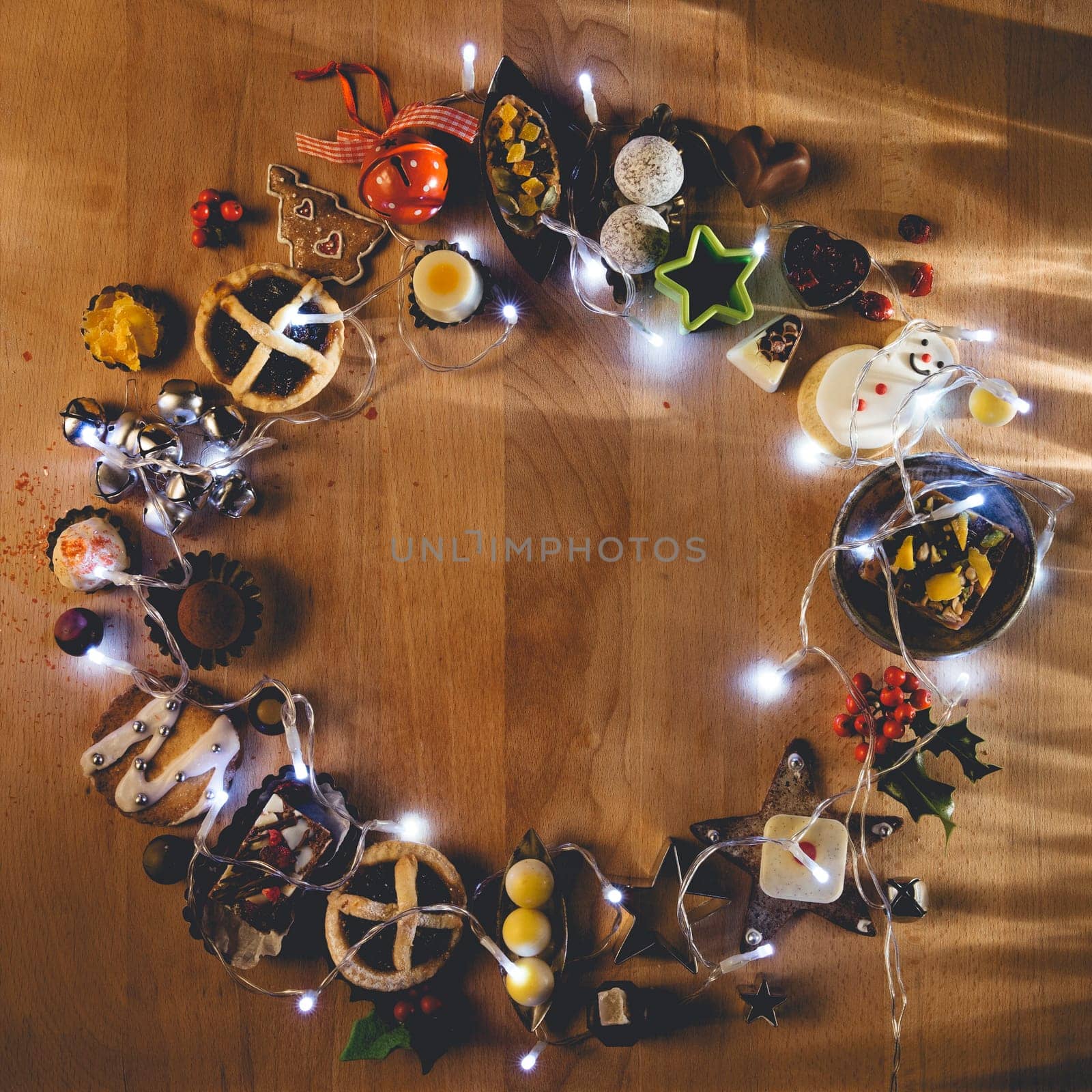 Christmas treats, accessories and fairy lights presented in a circle on a wooden chopping board.
