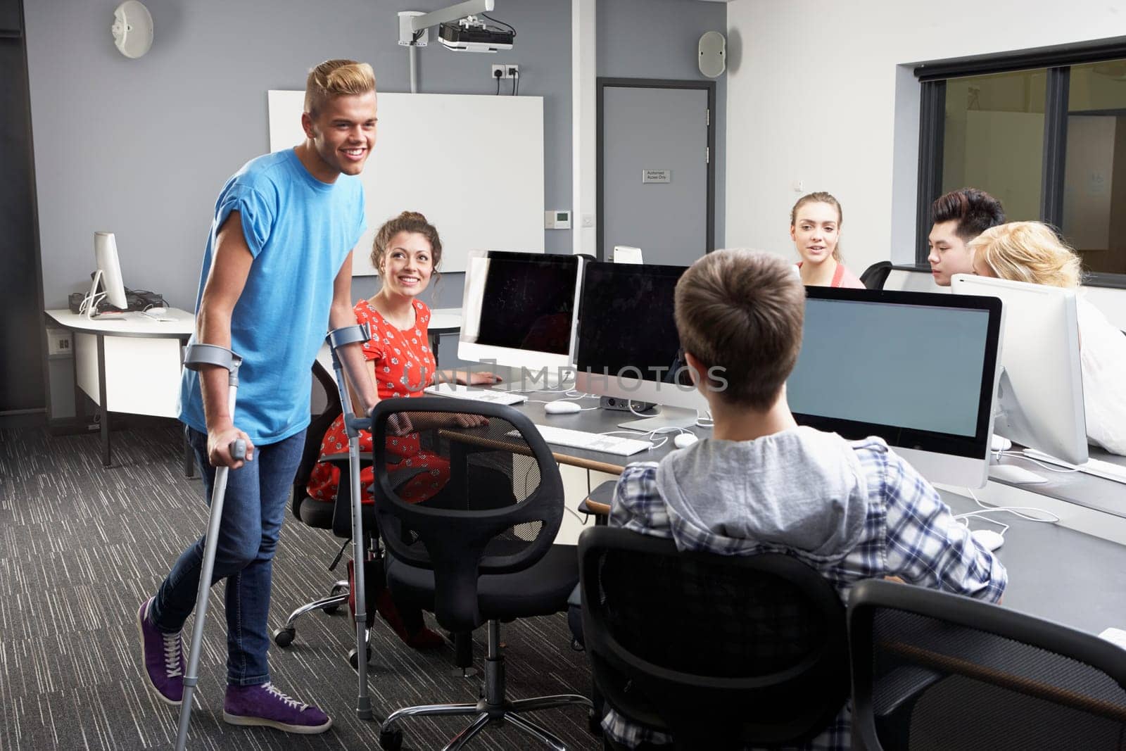 Male Pupil Walking On Crutches In Computer Class