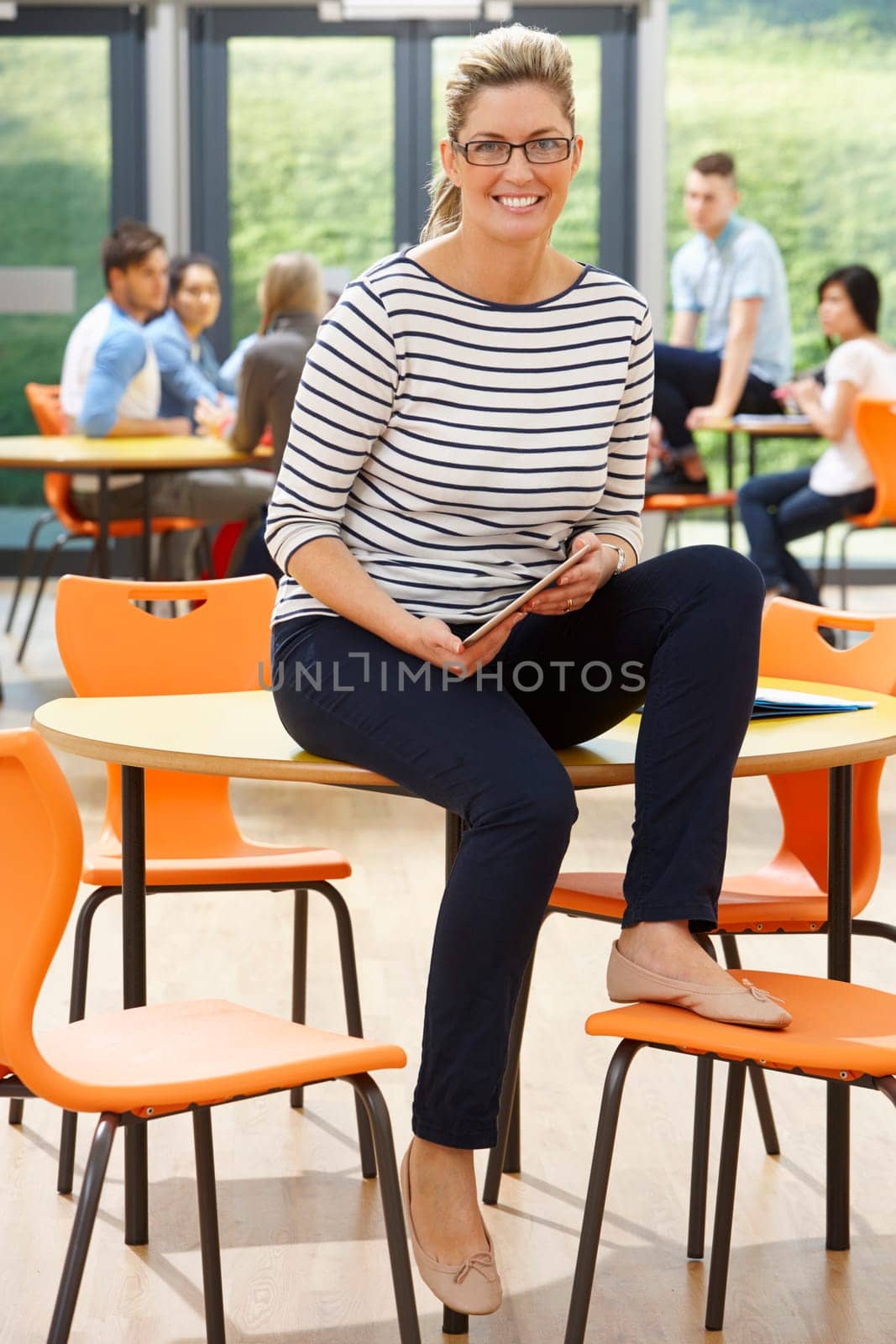Female Tutor Sitting In Classroom With Digital Tablet