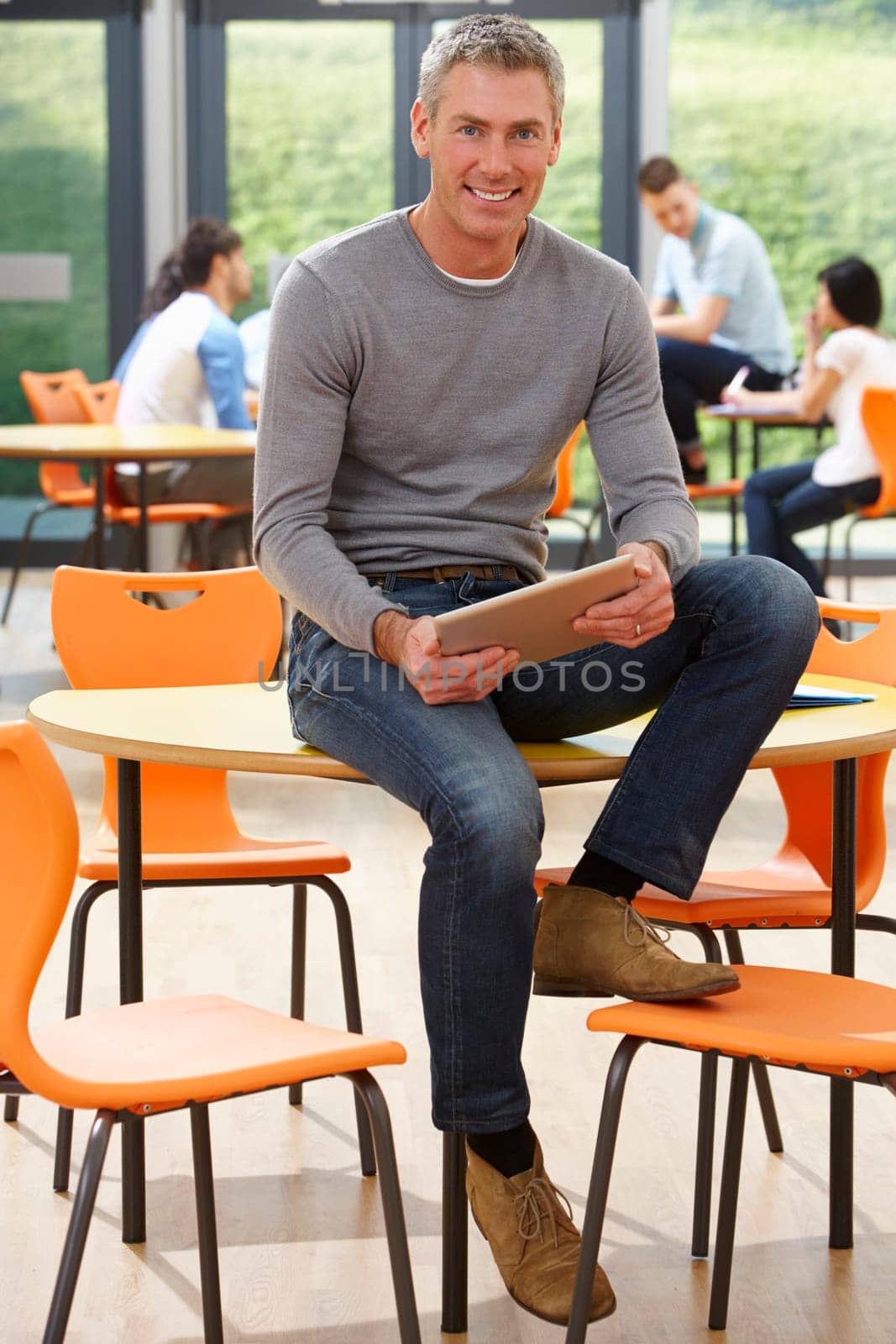 Male Tutor Sitting In Classroom With Digital Tablet