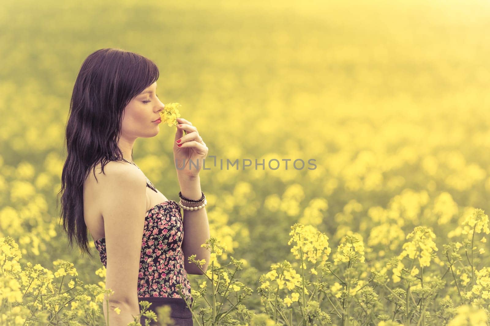 Attractive girl sniffs flowers on a meadow to the horizon in the sunshine in spring or summer. Photo of a series.