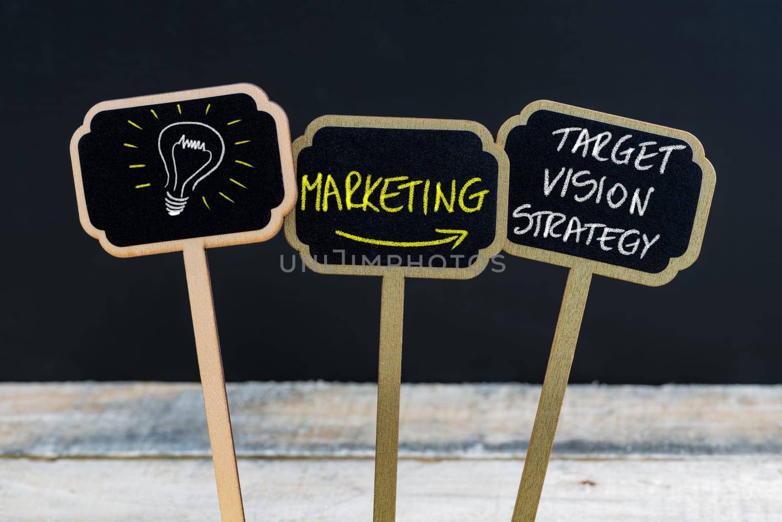 Concept message MARKETING - TARGET, VISION, STRATEGY and light bulb as symbol for idea written with chalk on wooden mini blackboard labels, defocused chalkboard and wood table in background