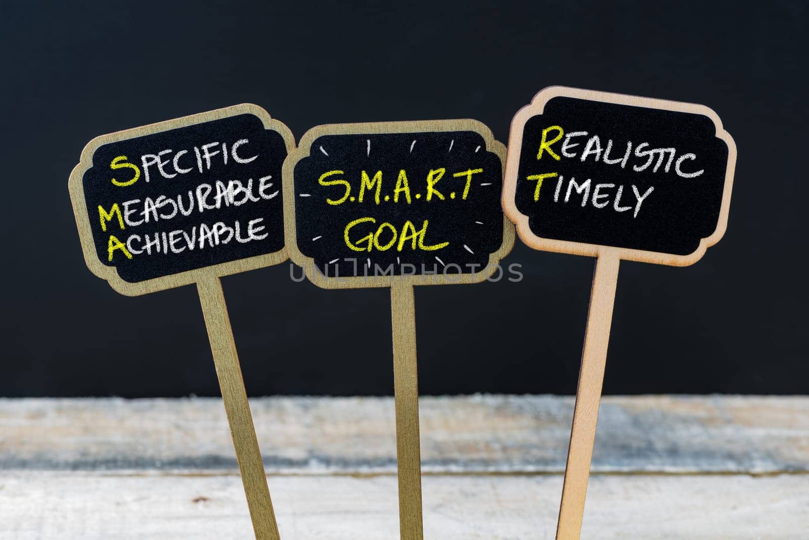 Concept message SMART GOAL written with chalk on wooden mini blackboard labels, defocused chalkboard and wood table in background