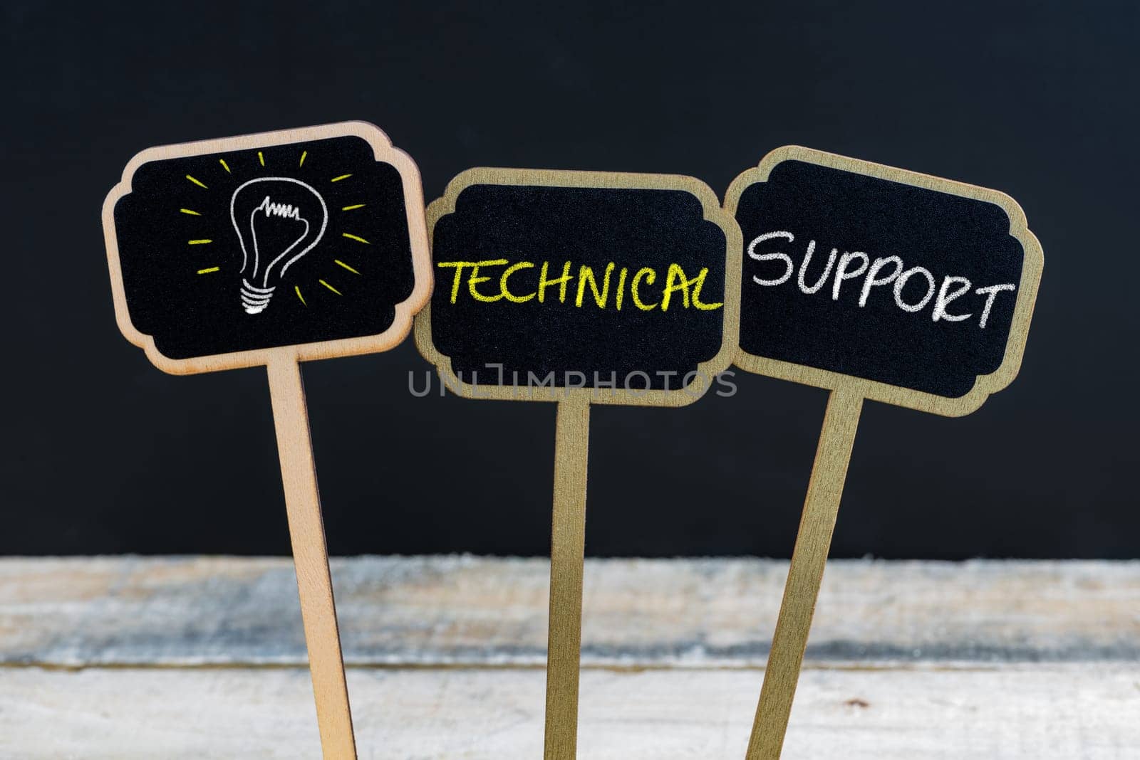 Concept message TECHNICAL SUPPORT and light bulb as symbol for idea written with chalk on wooden mini blackboard labels, defocused chalkboard and wood table in background