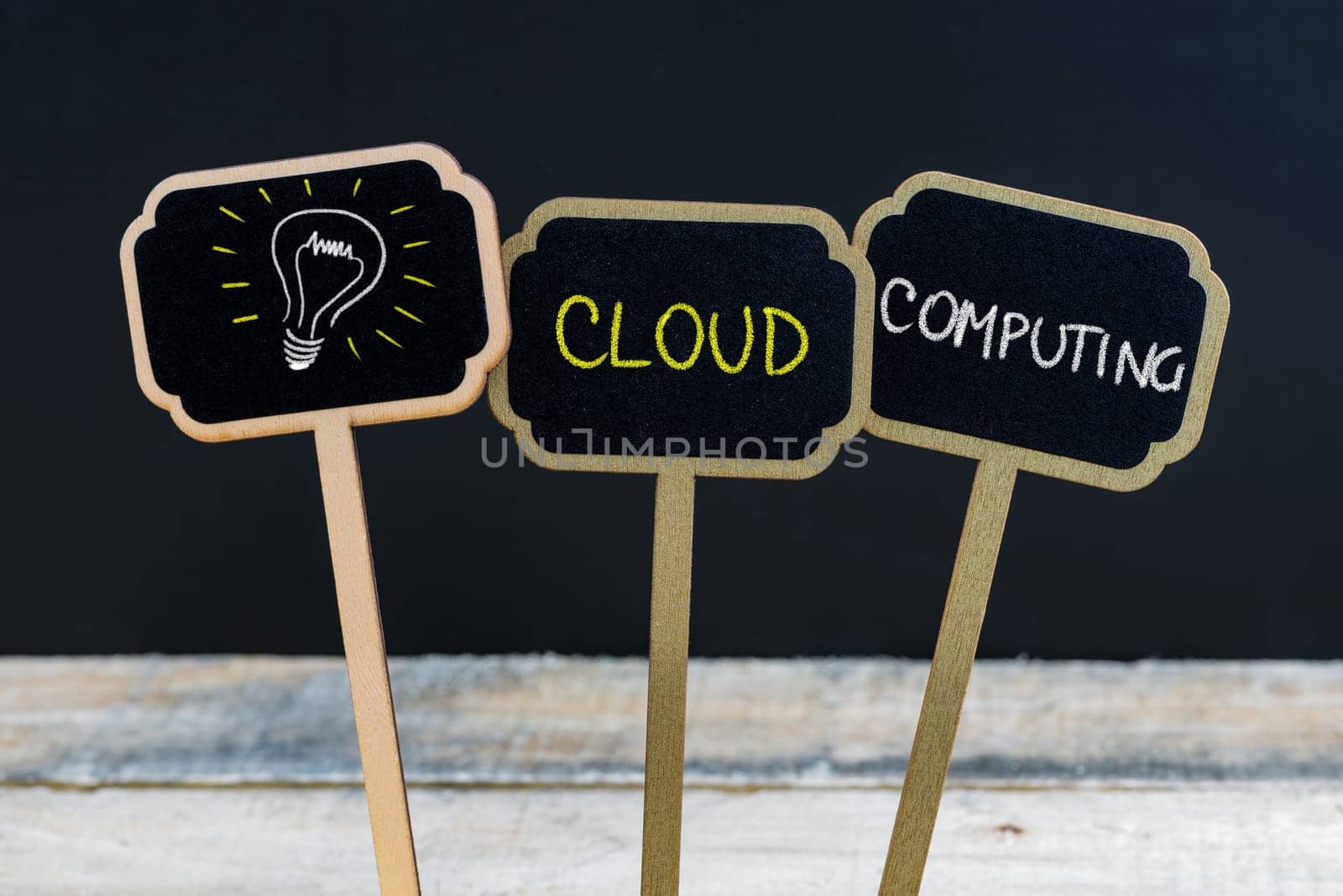 Concept message CLOUD COMPUTING and light bulb as symbol for idea written with chalk on wooden mini blackboard labels, defocused chalkboard and wood table in background