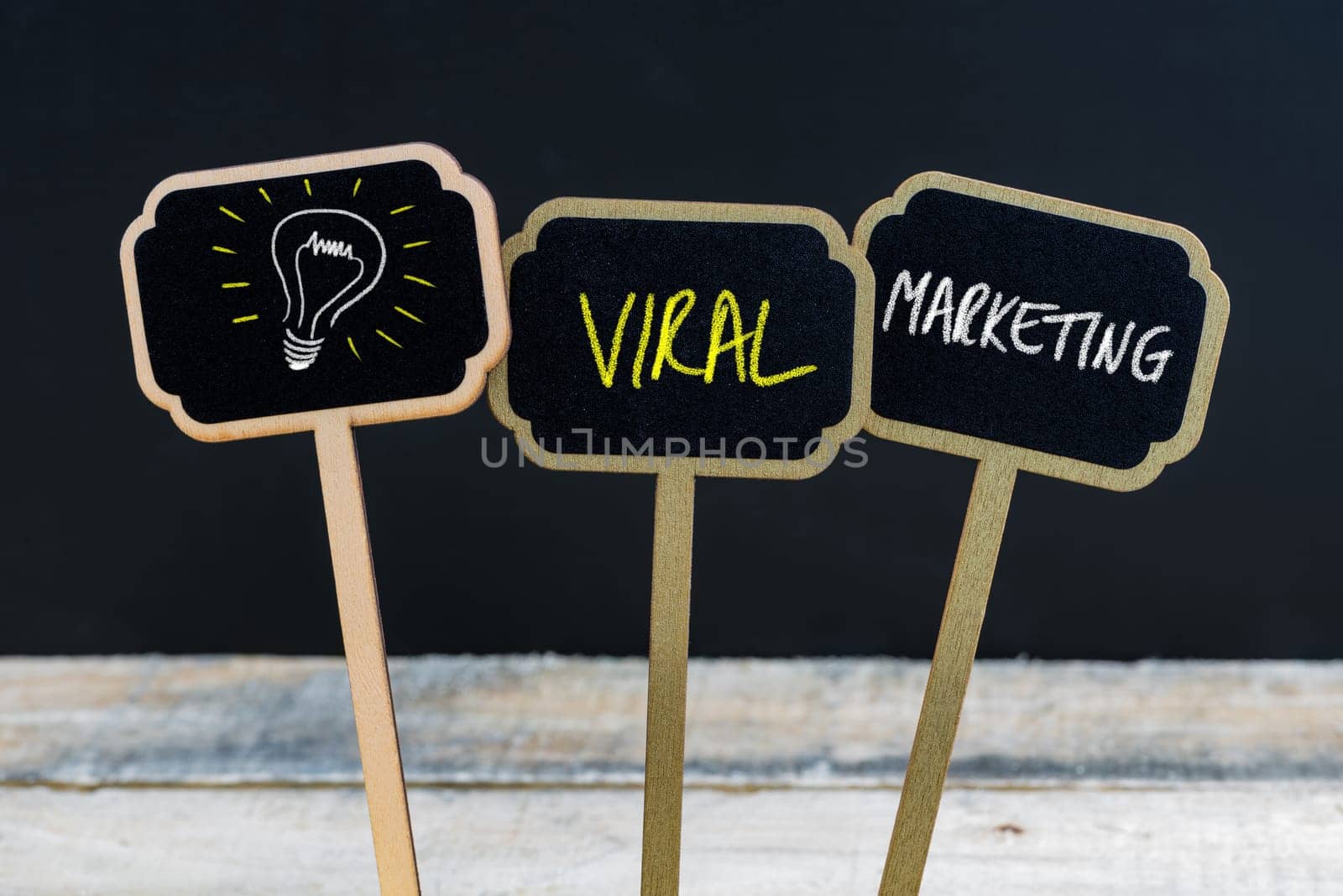 Concept message VIRAL MARKETING and light bulb as symbol for idea written with chalk on wooden mini blackboard labels, defocused chalkboard and wood table in background