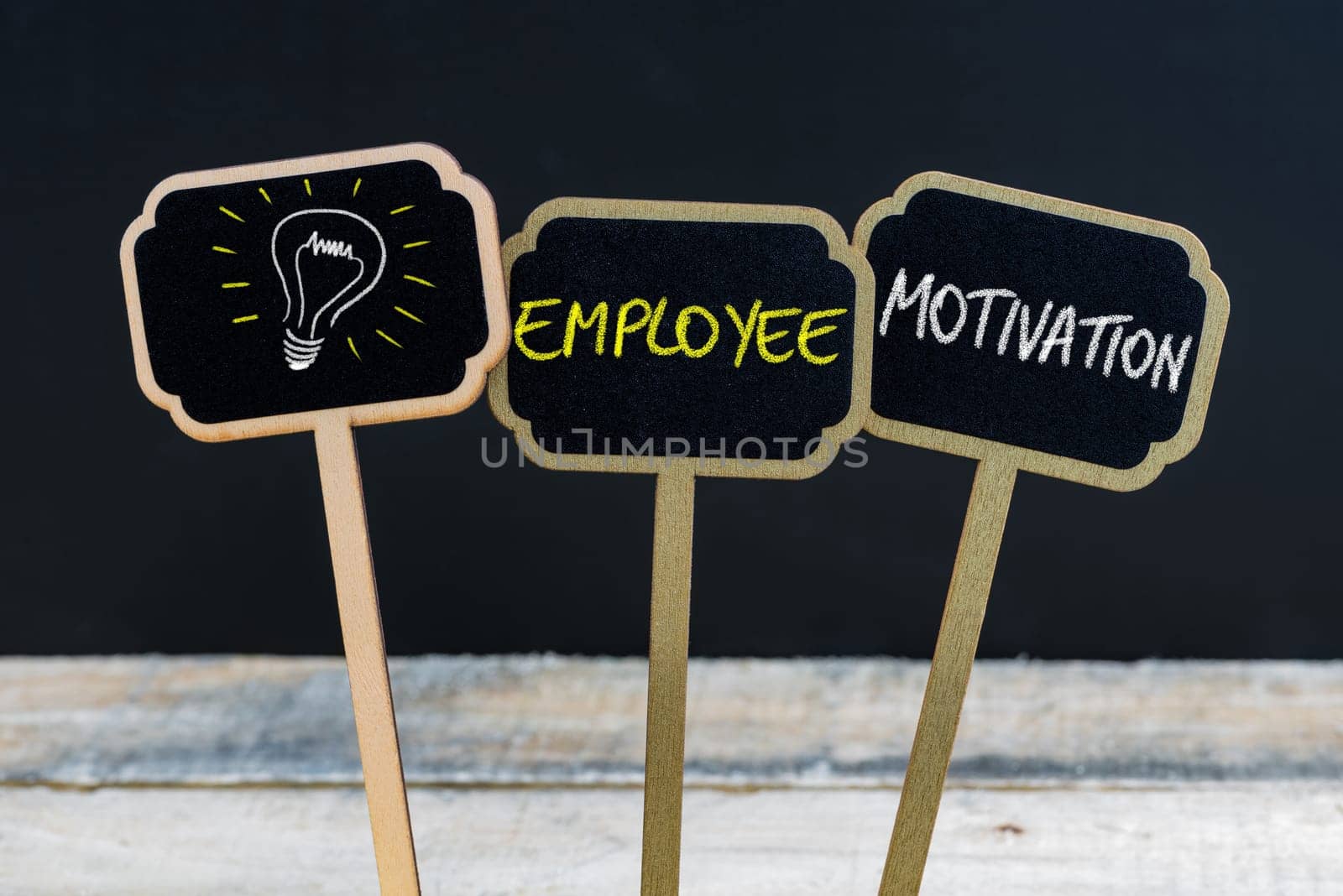 Concept message EMPLOYEE MOTIVATION and light bulb as symbol for idea written with chalk on wooden mini blackboard labels, defocused chalkboard and wood table in background
