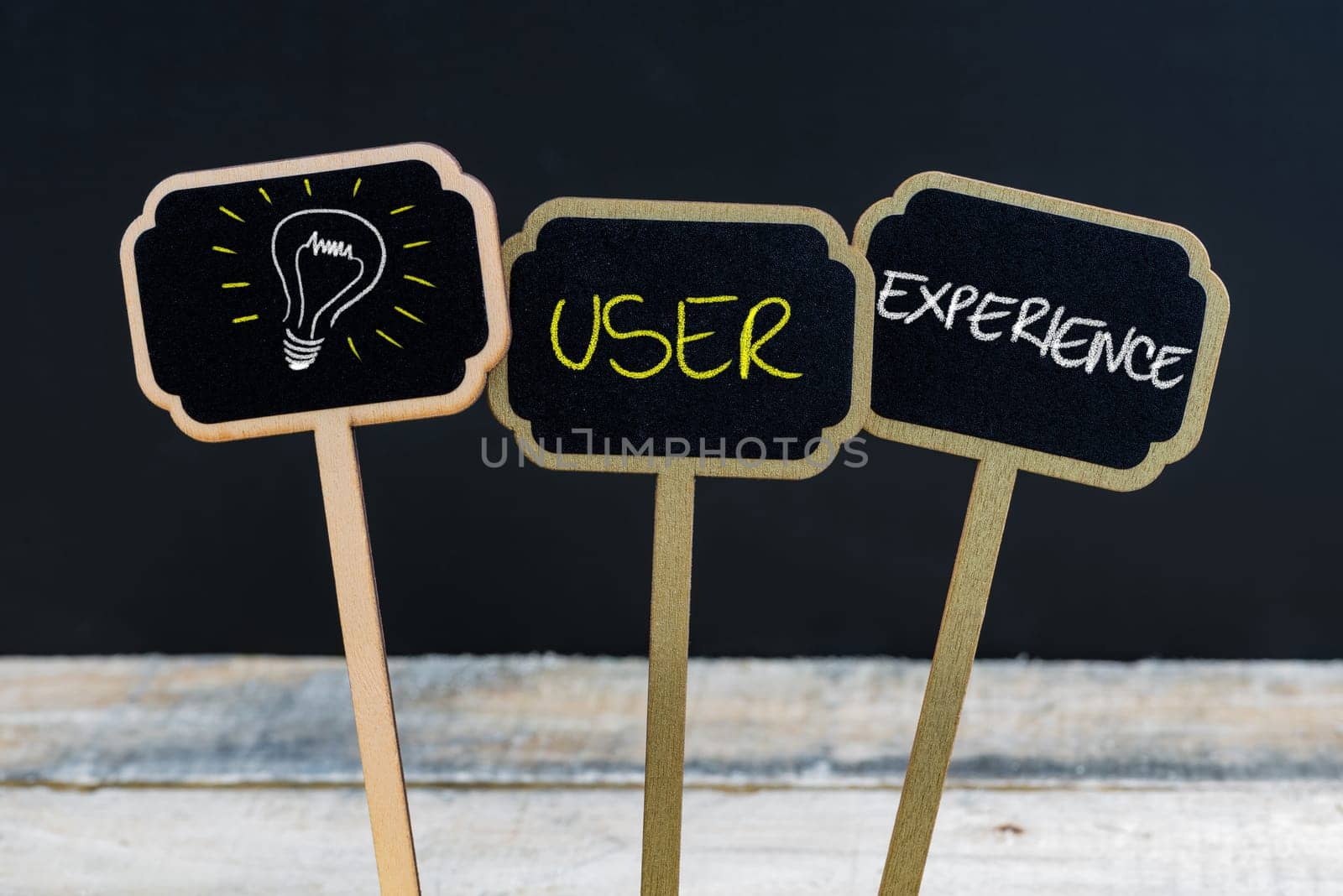 Concept message USER EXPERIENCE and light bulb as symbol for idea written with chalk on wooden mini blackboard labels, defocused chalkboard and wood table in background