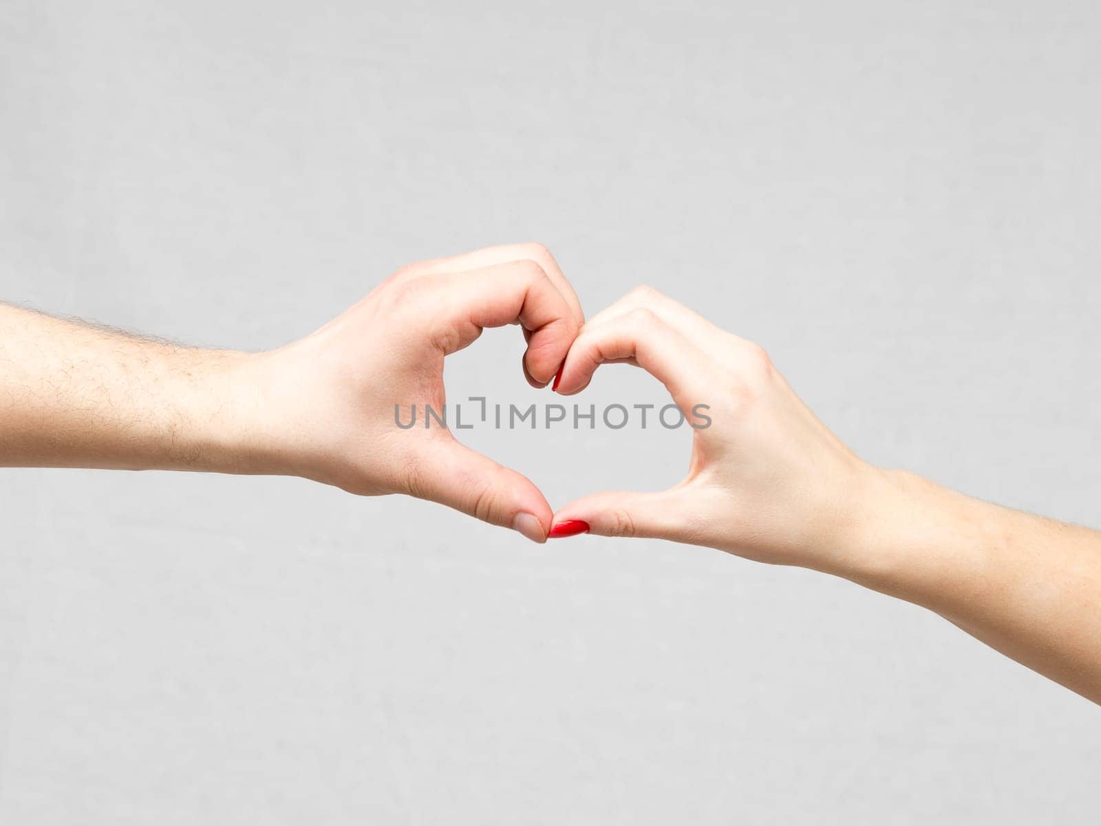 Female and Male Hands Making a Heart Shape on a gray background.