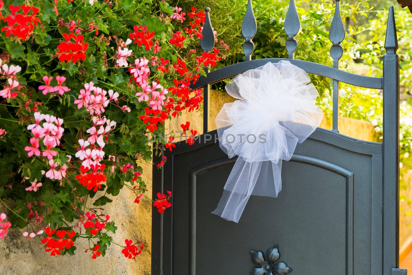 View of a bridal bow put on an iron gate with colorful flowers on the left