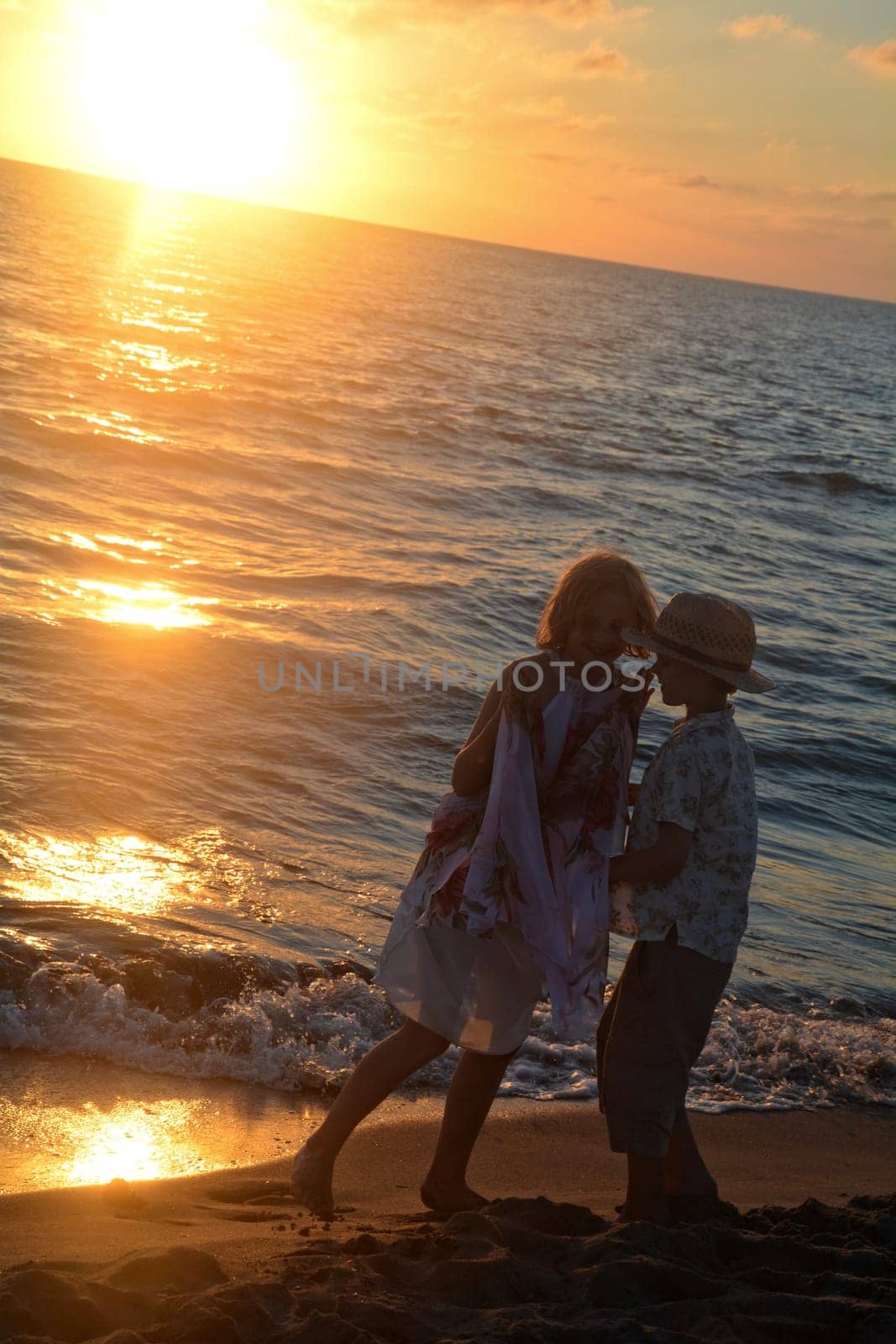 Girl in dress and boy playing at sunset on the beach