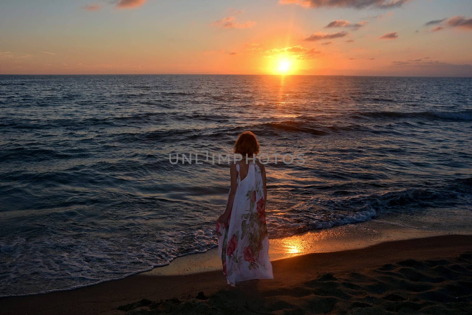 Girl in a long dress stands on the sea beach at sunset,with a view of the sun