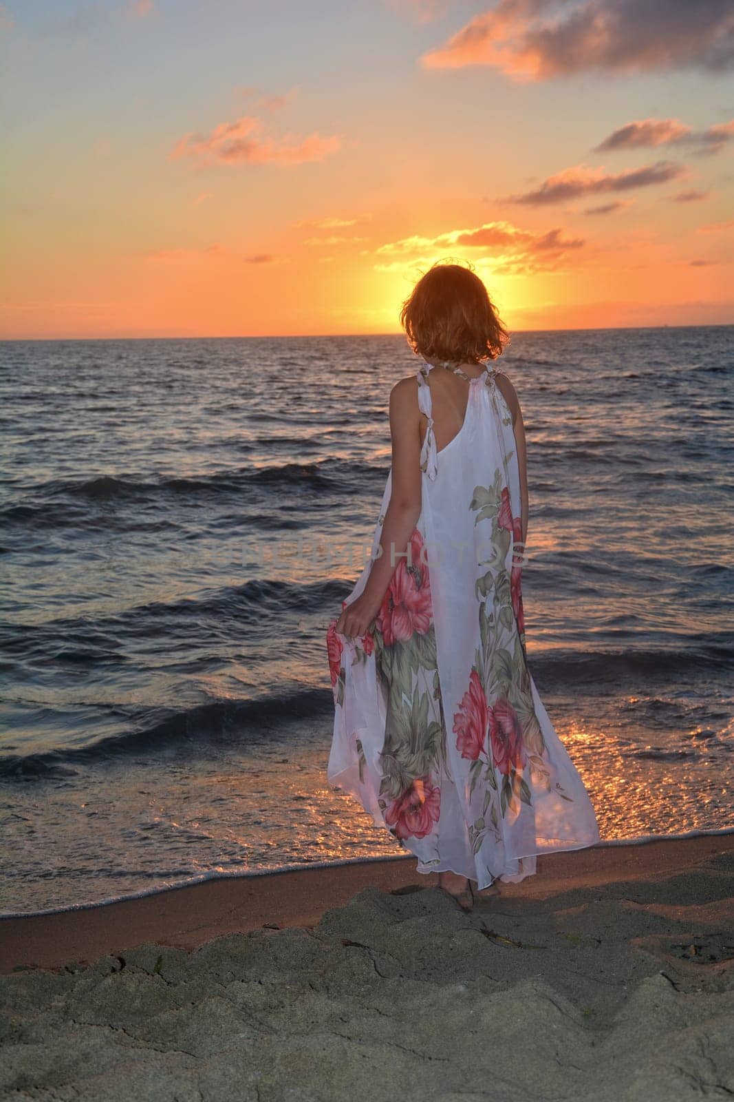Girl in a long dress stands on the sea beach at sunset,with a view to the sun,head covers the sun