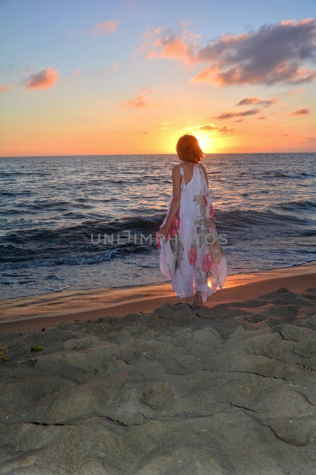 Girl in a long dress stands on the sea beach at sunset,with a view to the sun,head covers the sun